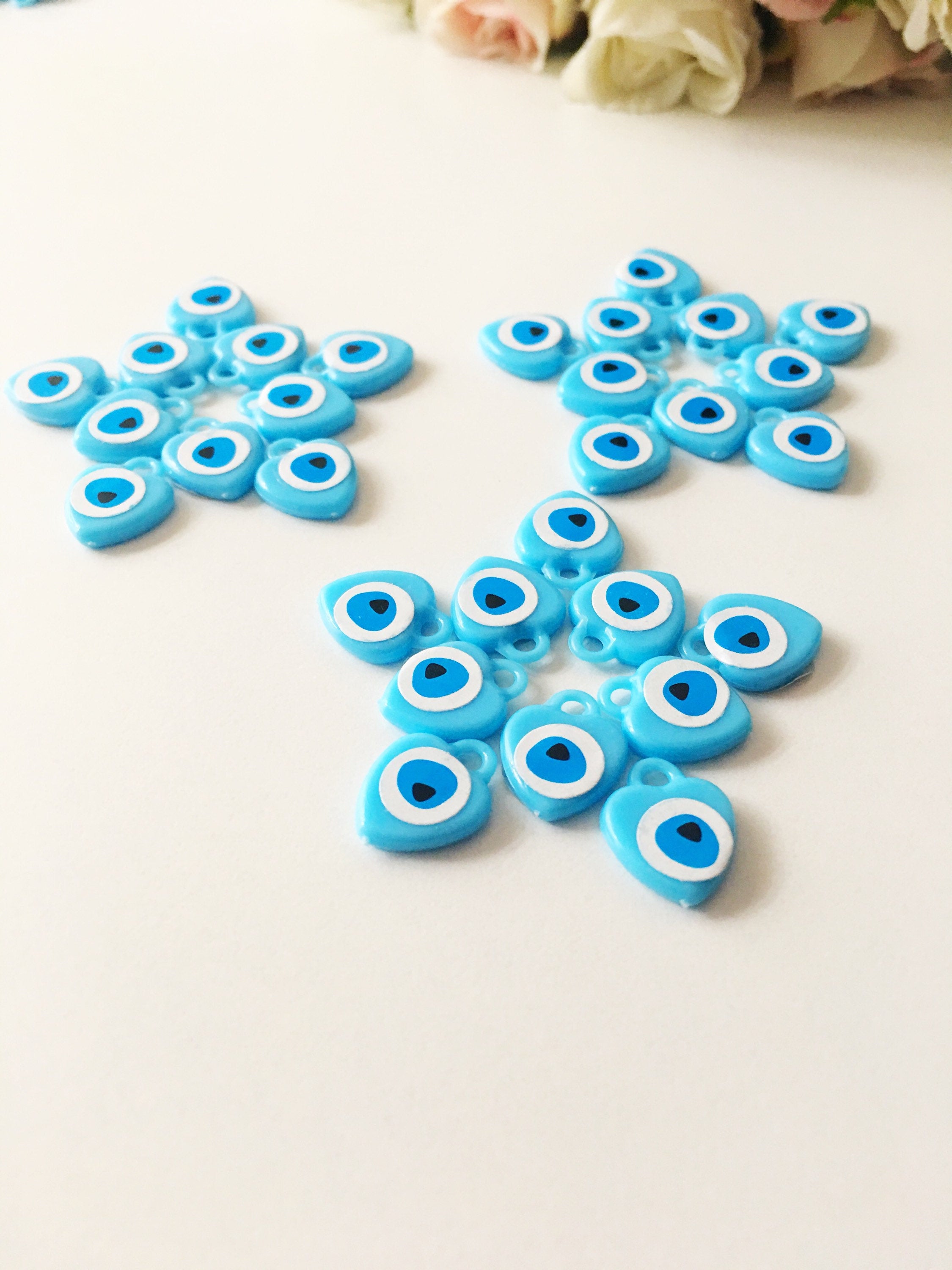 A collection of 100 turquoise evil eye charms made from resin, showcasing their vibrant blue color and unique design, perfect for wedding and baby shower favors.