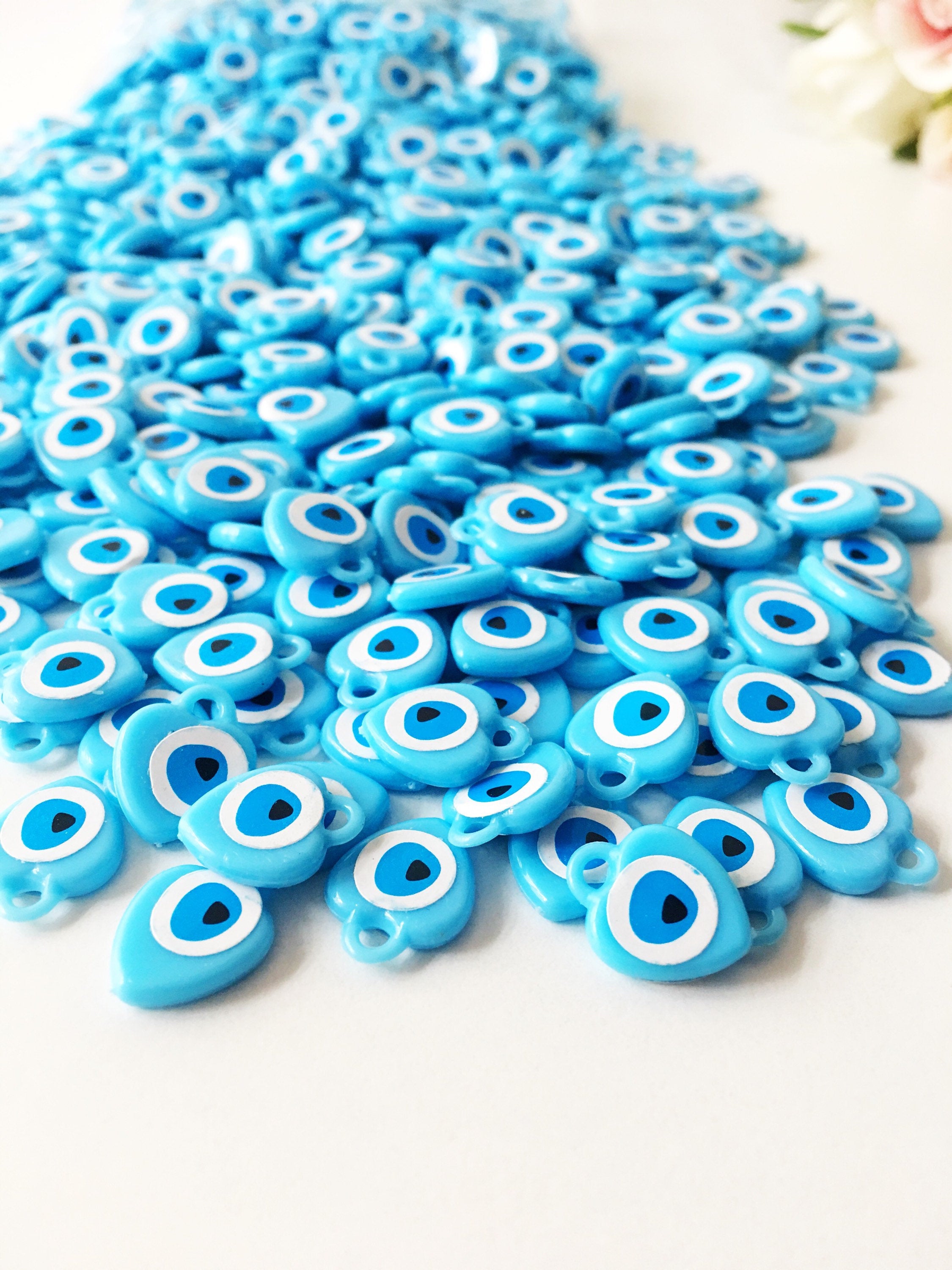 A collection of 100 turquoise evil eye charms made from resin, showcasing their vibrant blue color and unique design, perfect for wedding and baby shower favors.