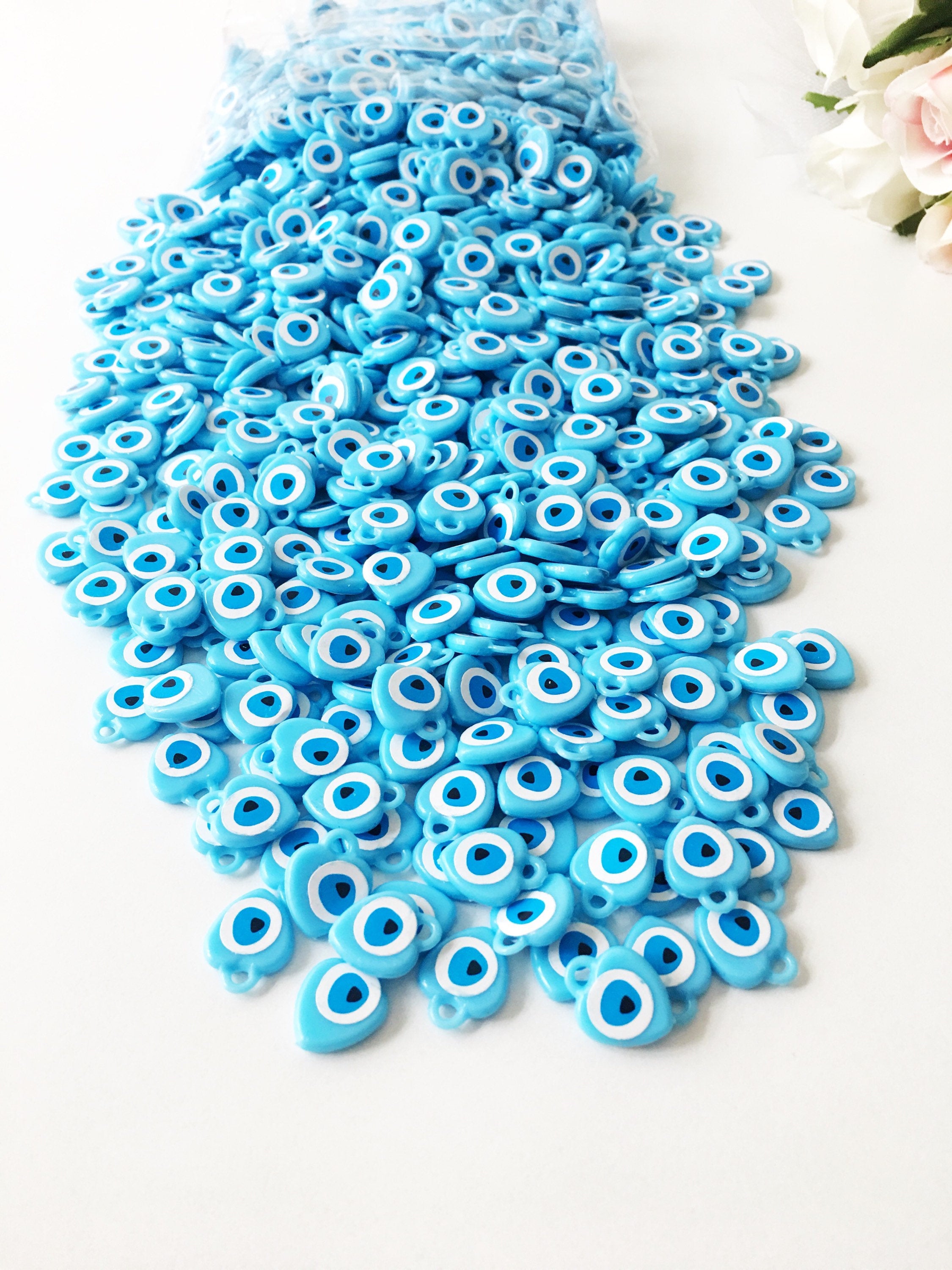 A collection of 100 turquoise evil eye charms made from resin, showcasing their vibrant blue color and unique design, perfect for wedding and baby shower favors.