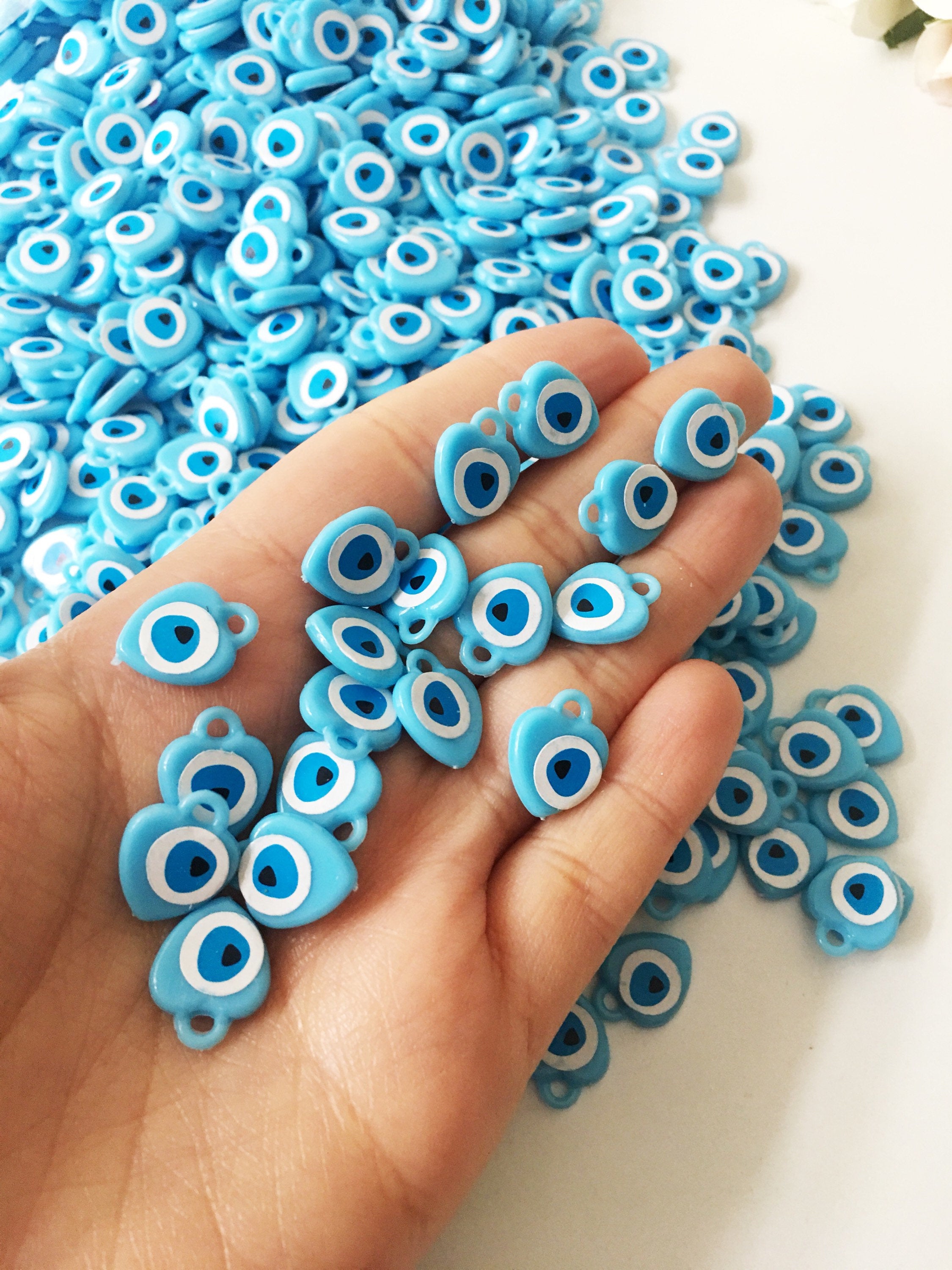 A collection of 100 turquoise evil eye charms made from resin, showcasing their vibrant blue color and unique design, perfect for wedding and baby shower favors.
