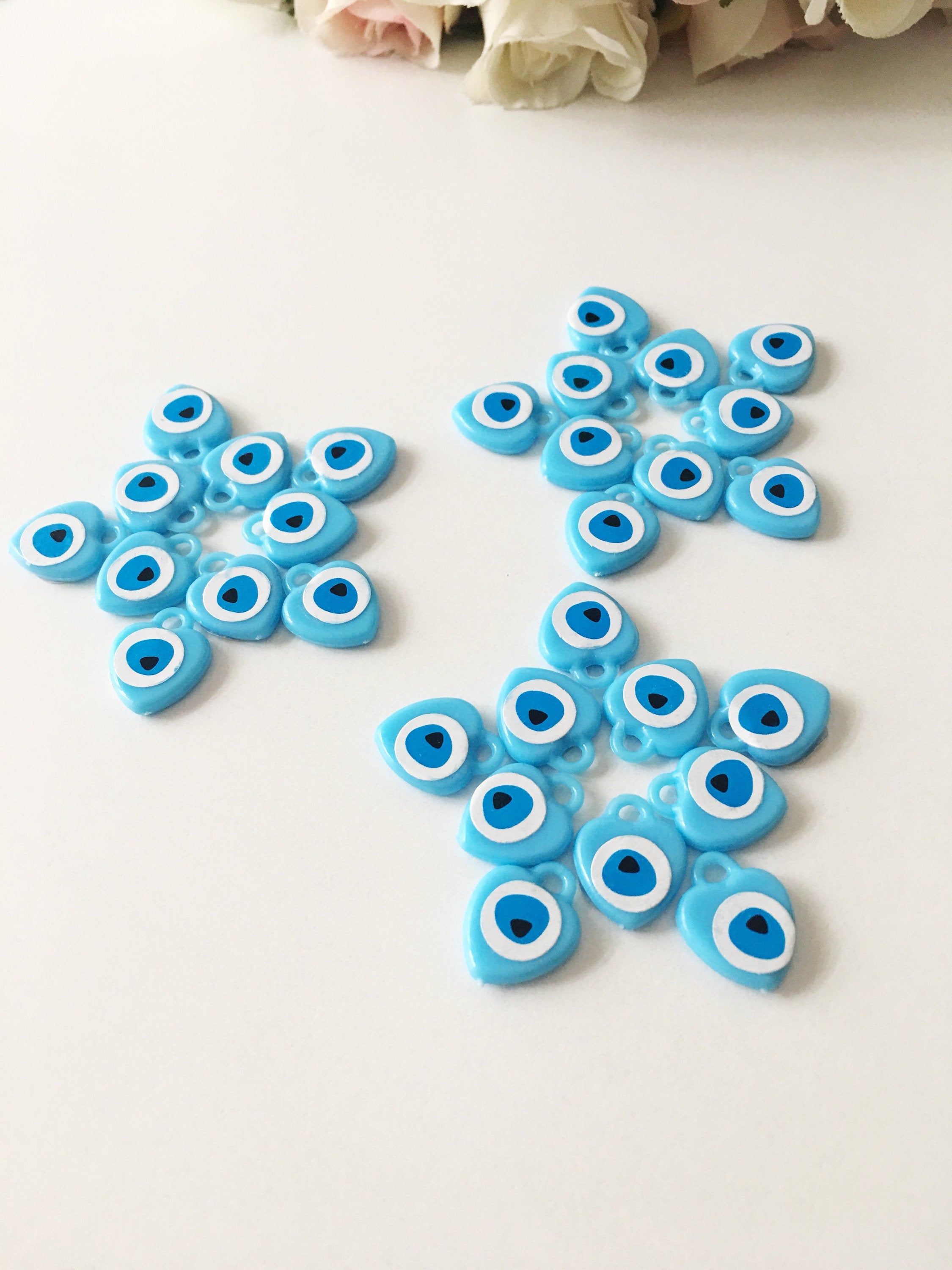 A collection of 100 turquoise evil eye charms made from resin, showcasing their vibrant blue color and unique design, perfect for wedding and baby shower favors.