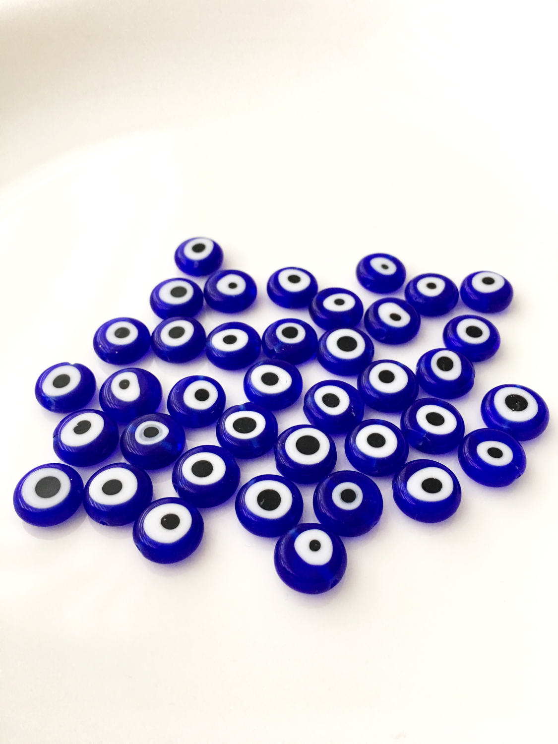 A collection of 120 blue glass evil eye beads in various sizes from 6mm to 12mm, showcasing their unique handmade designs.