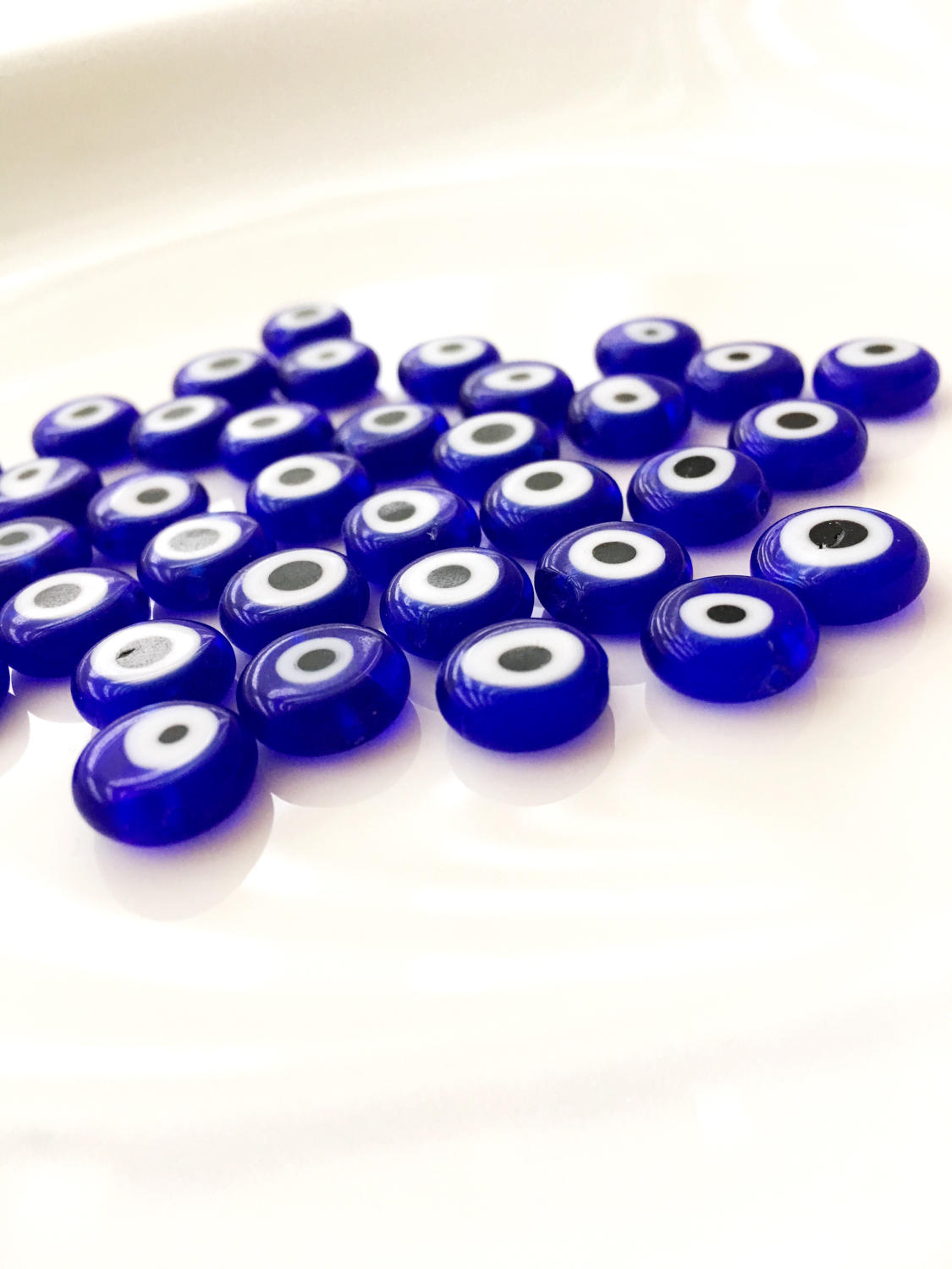 A collection of 120 blue glass evil eye beads in various sizes from 6mm to 12mm, showcasing their unique handmade designs.