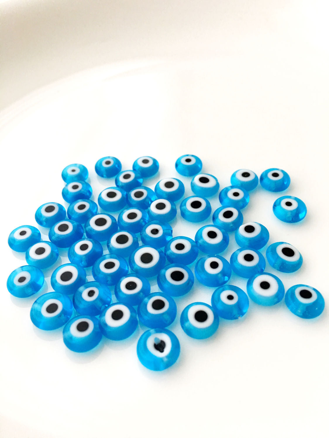 A collection of 120 turquoise glass evil eye beads in various sizes from 6mm to 12mm, showcasing their unique handmade designs.