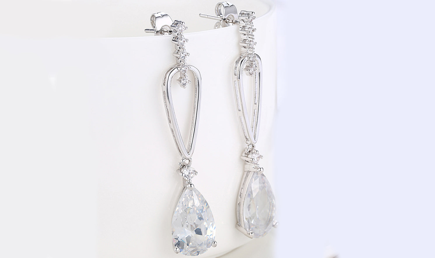 Elegant 14K white gold plated dangling earrings featuring pear cut white sapphires, showcasing their stunning design and craftsmanship.