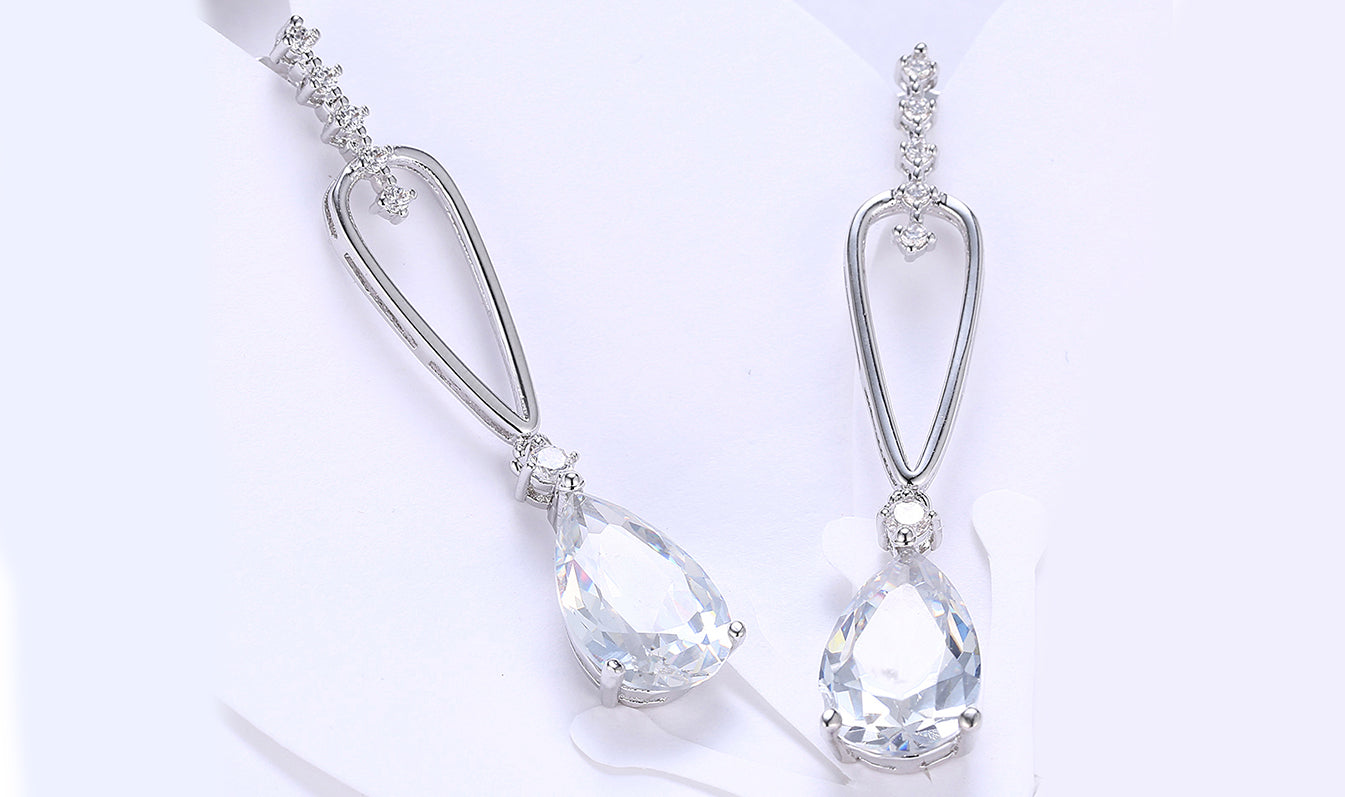 Elegant 14K white gold plated dangling earrings featuring pear cut white sapphires, showcasing their stunning design and craftsmanship.