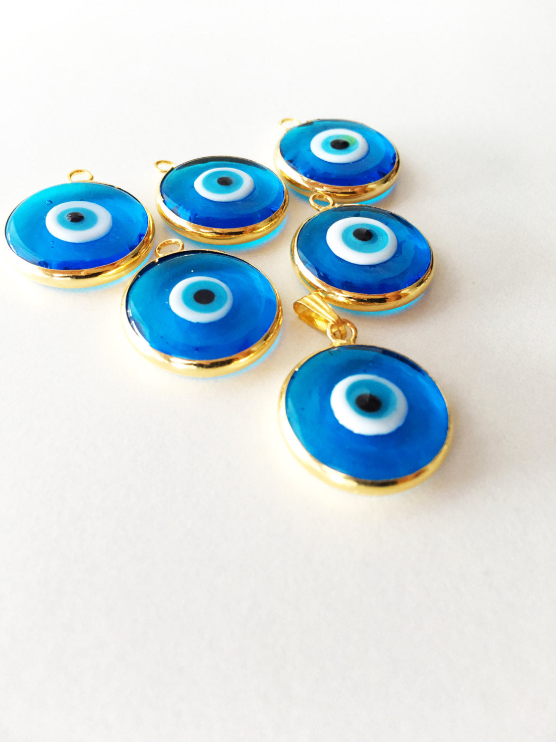 Two gold plated evil eye pendants with turquoise designs, showcasing intricate glass craftsmanship and 24K matte gold finish.