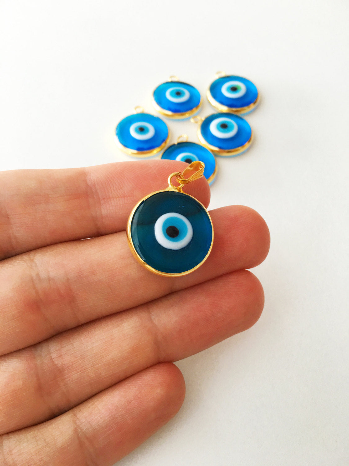 Two gold plated evil eye pendants with turquoise designs, showcasing intricate glass craftsmanship and 24K matte gold finish.