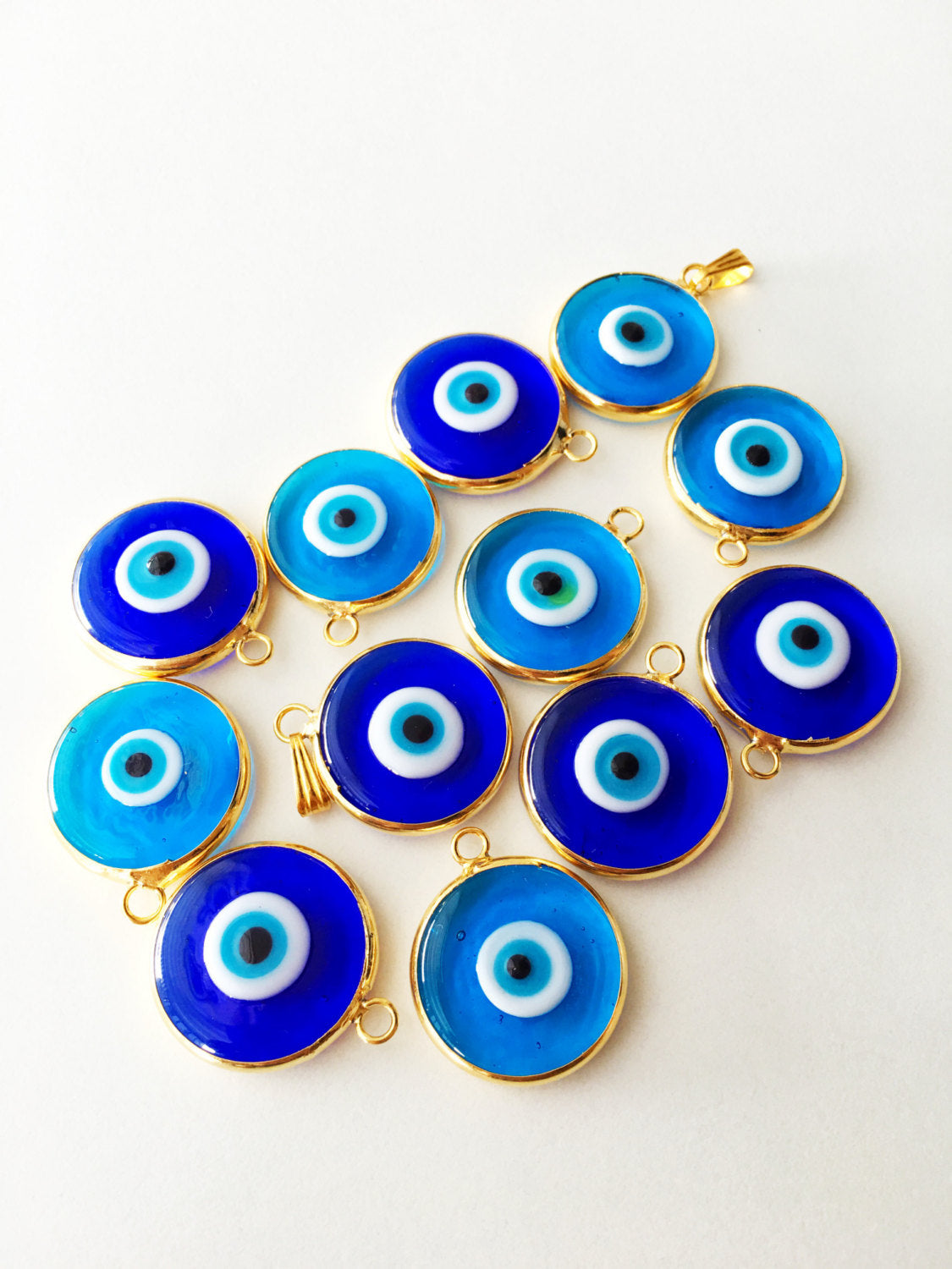 Two gold plated evil eye pendants with turquoise designs, showcasing intricate glass craftsmanship and 24K matte gold finish.