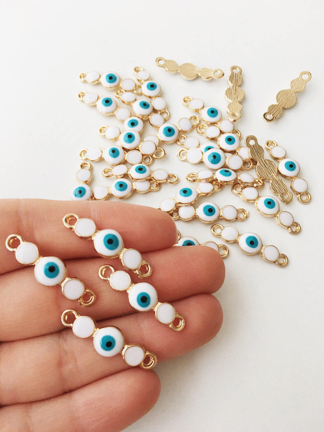 Three gold plated evil eye charms featuring white enamel and dark blue options, ideal for jewelry making.
