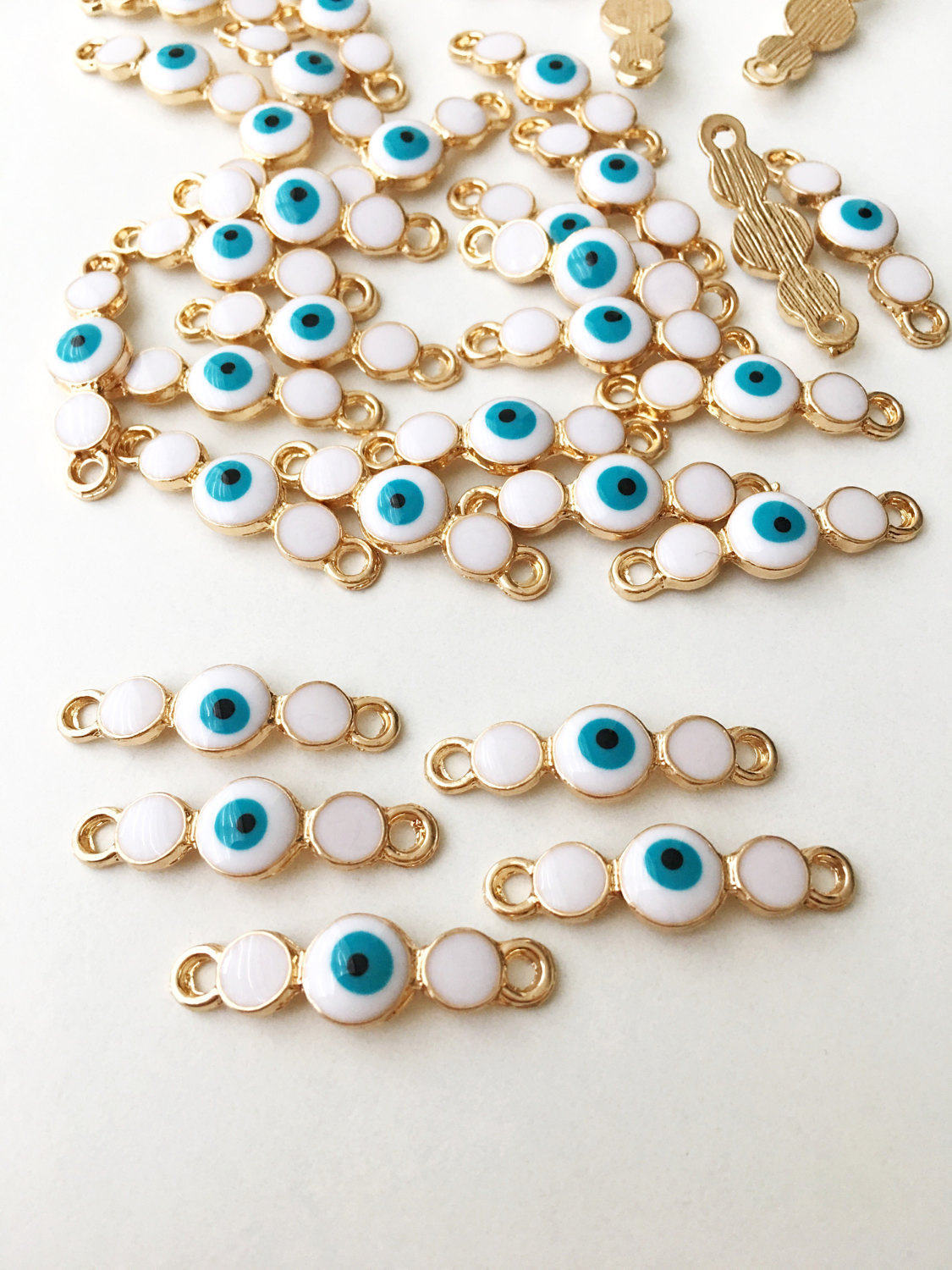 Three gold plated evil eye charms featuring white enamel and dark blue options, ideal for jewelry making.