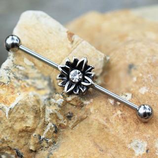 A 316L stainless steel industrial barbell featuring a black flower design with a clear cubic zirconia center, showcasing its intricate details.