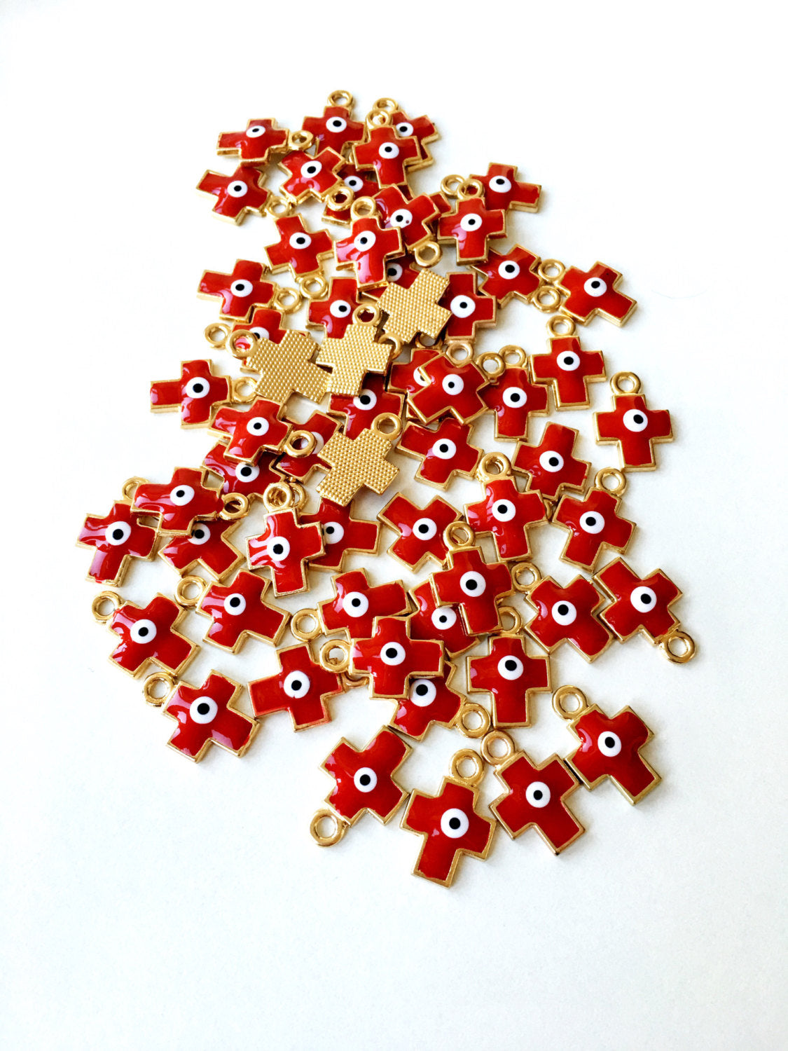 Five pieces of cross evil eye charms with red enamel and gold plating, showcasing intricate designs and vibrant colors.