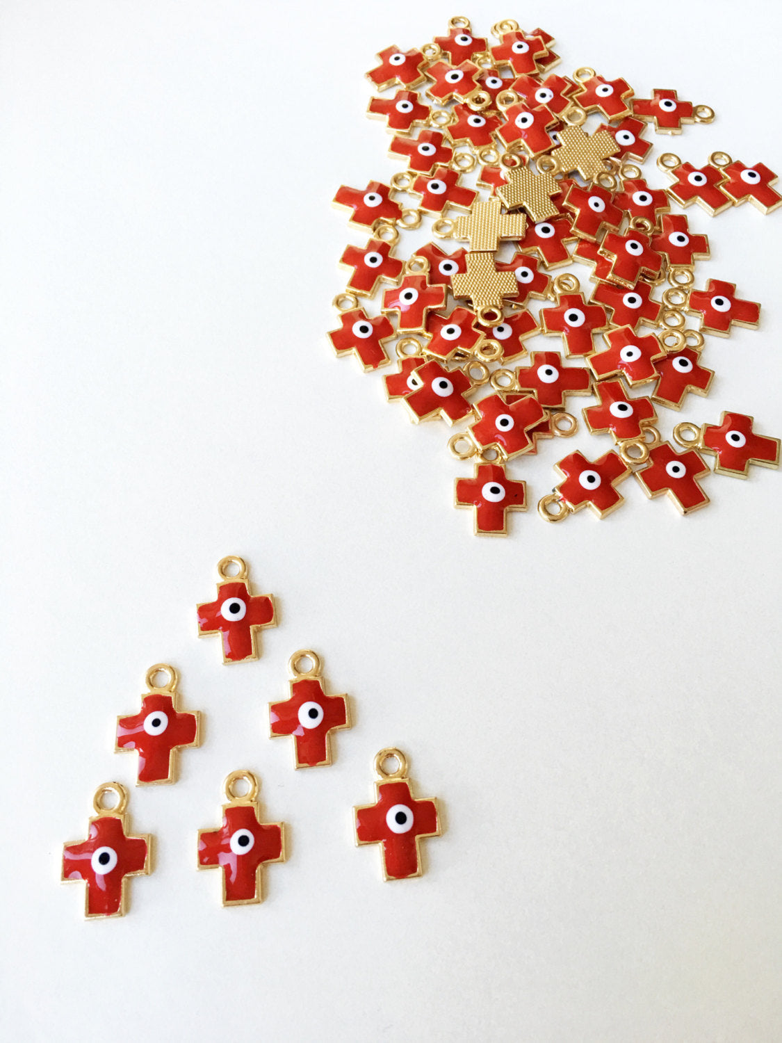 Five pieces of cross evil eye charms with red enamel and gold plating, showcasing intricate designs and vibrant colors.