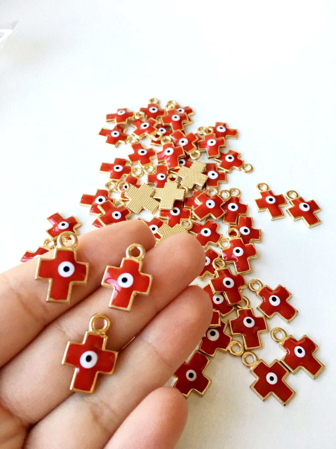 Five pieces of cross evil eye charms with red enamel and gold plating, showcasing intricate designs and vibrant colors.