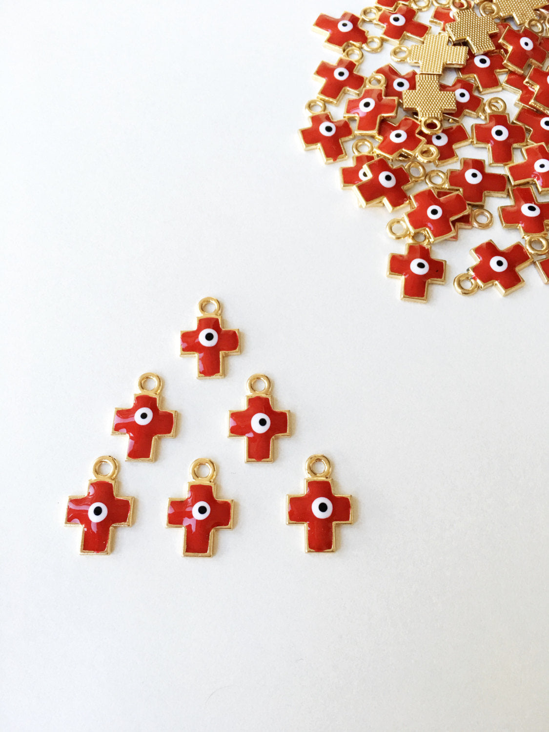 Five pieces of cross evil eye charms with red enamel and gold plating, showcasing intricate designs and vibrant colors.