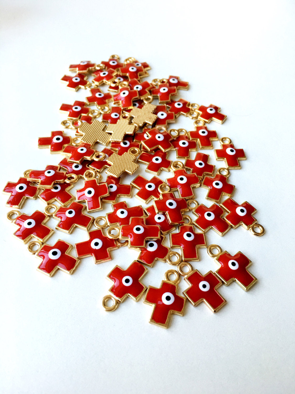 Five pieces of cross evil eye charms with red enamel and gold plating, showcasing intricate designs and vibrant colors.