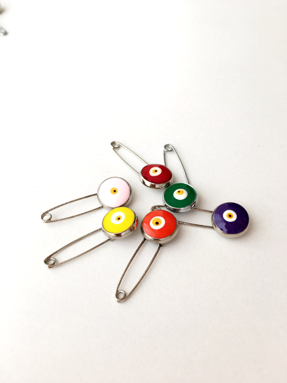 Set of 5 evil eye safety pins in various colors, featuring a big enamel evil eye charm on a silver plated safety pin.