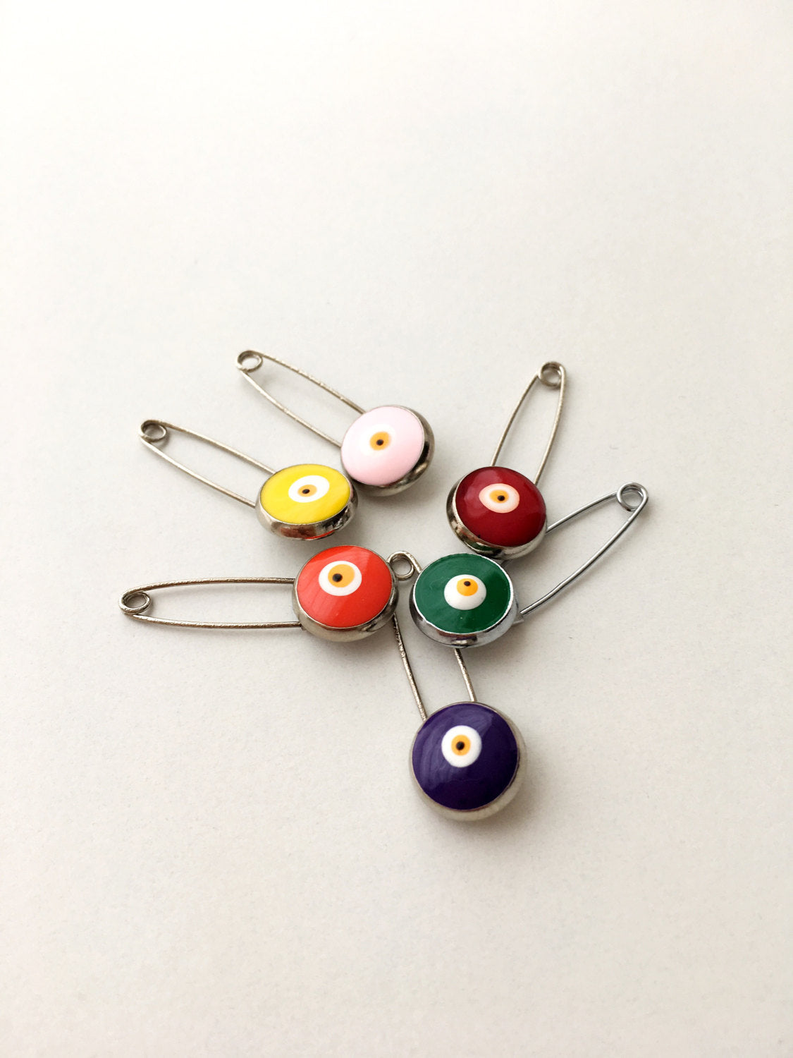Set of 5 evil eye safety pins in various colors, featuring a big enamel evil eye charm on a silver plated safety pin.