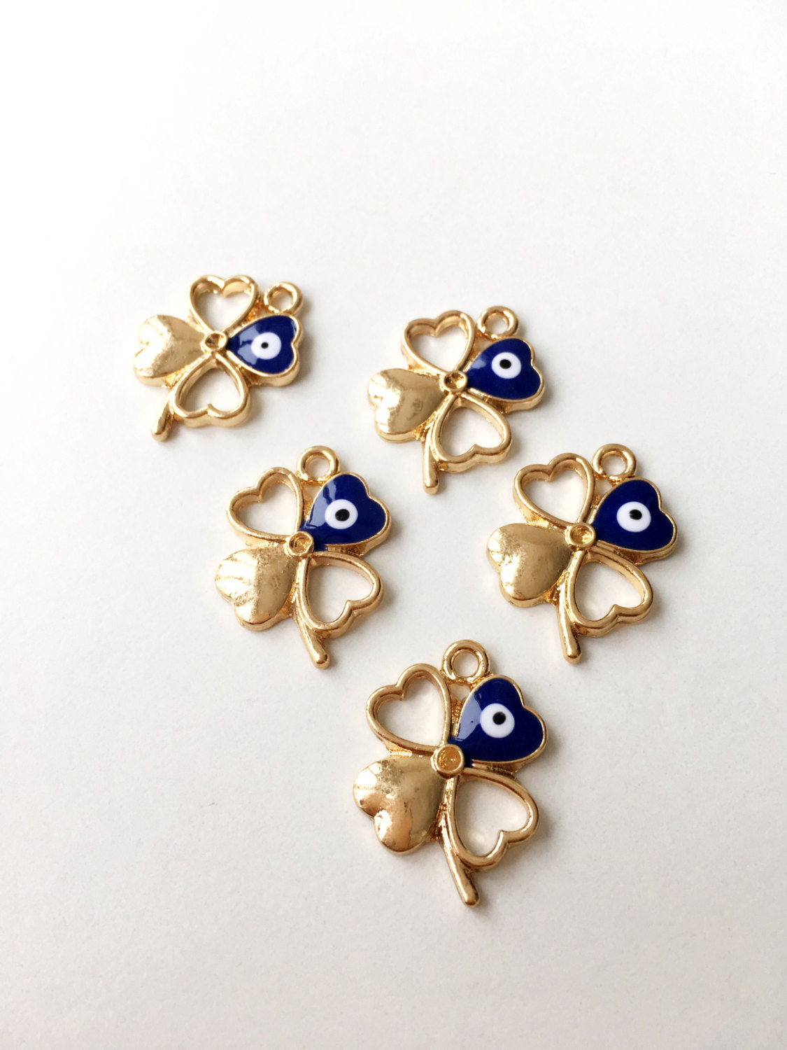 Five gold plated four leaf clover evil eye pendants, showcasing intricate designs and a protective charm.