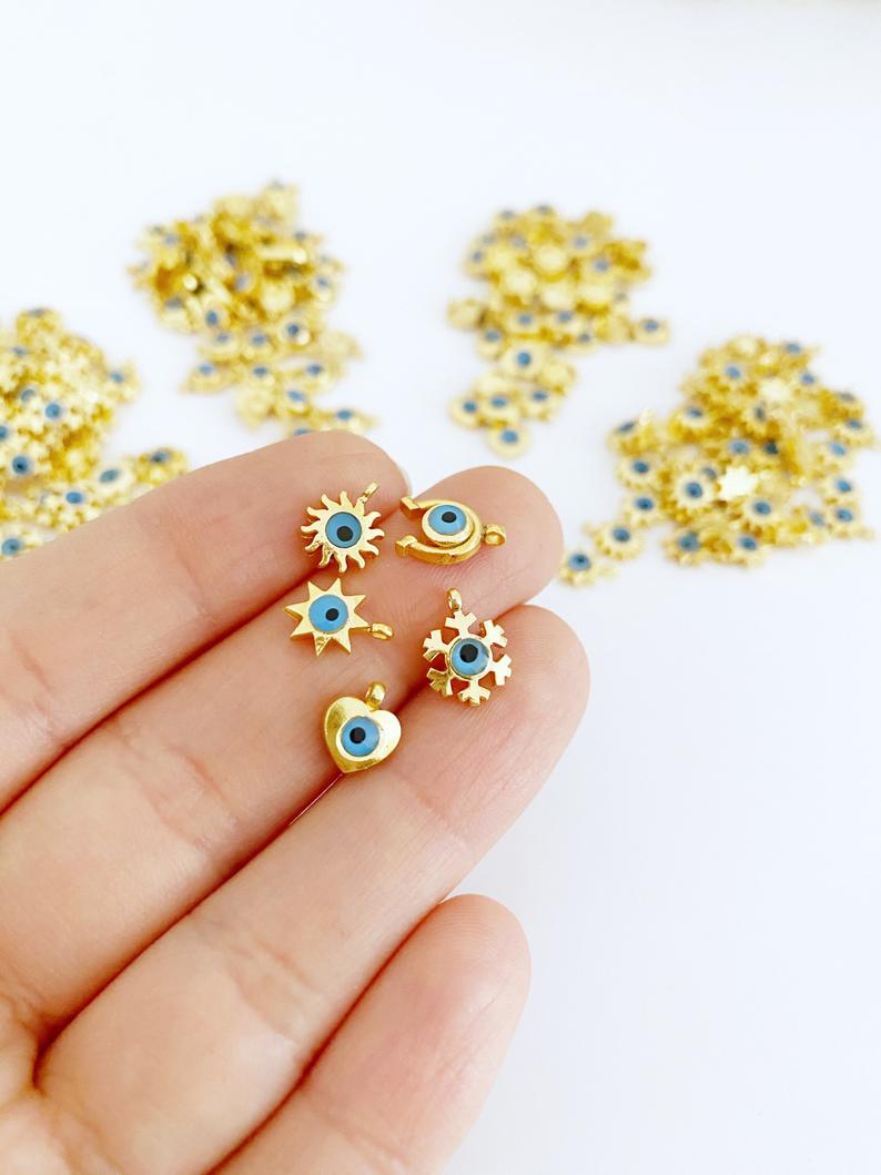 Five gold mini evil eye charms featuring heart, star, horseshoe, and snowflake designs, perfect for DIY jewelry projects.