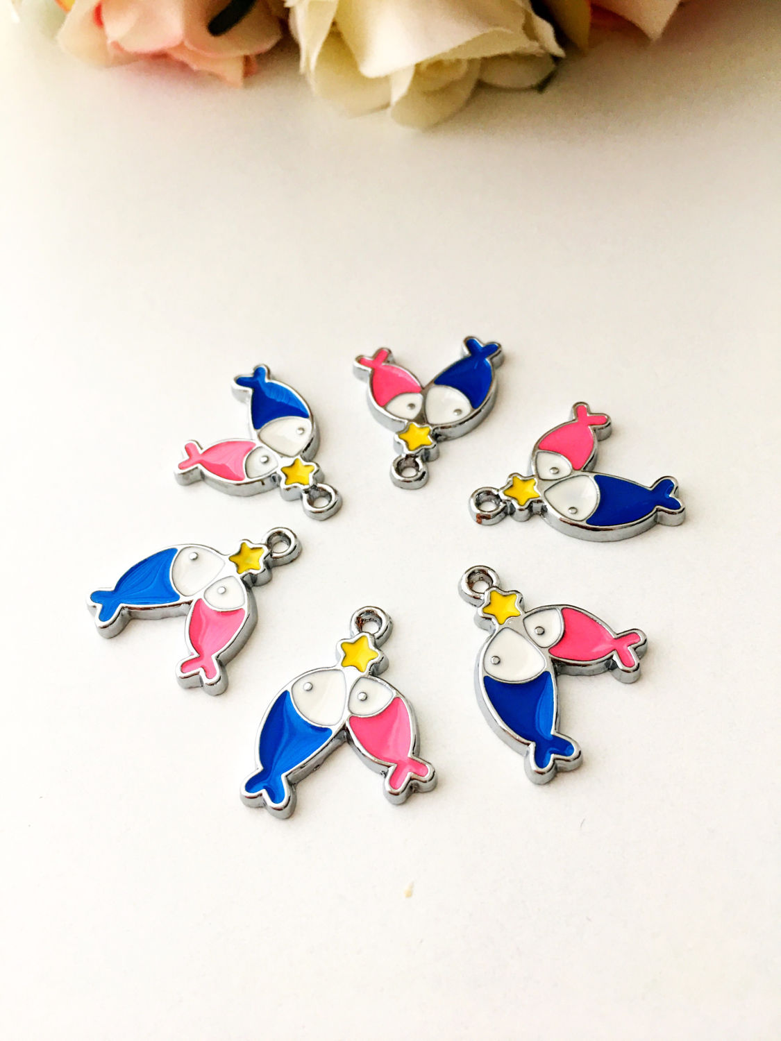 Five tiny fish charms in pink and blue, along with a star charm, made from enamel and brass, perfect for jewelry making.