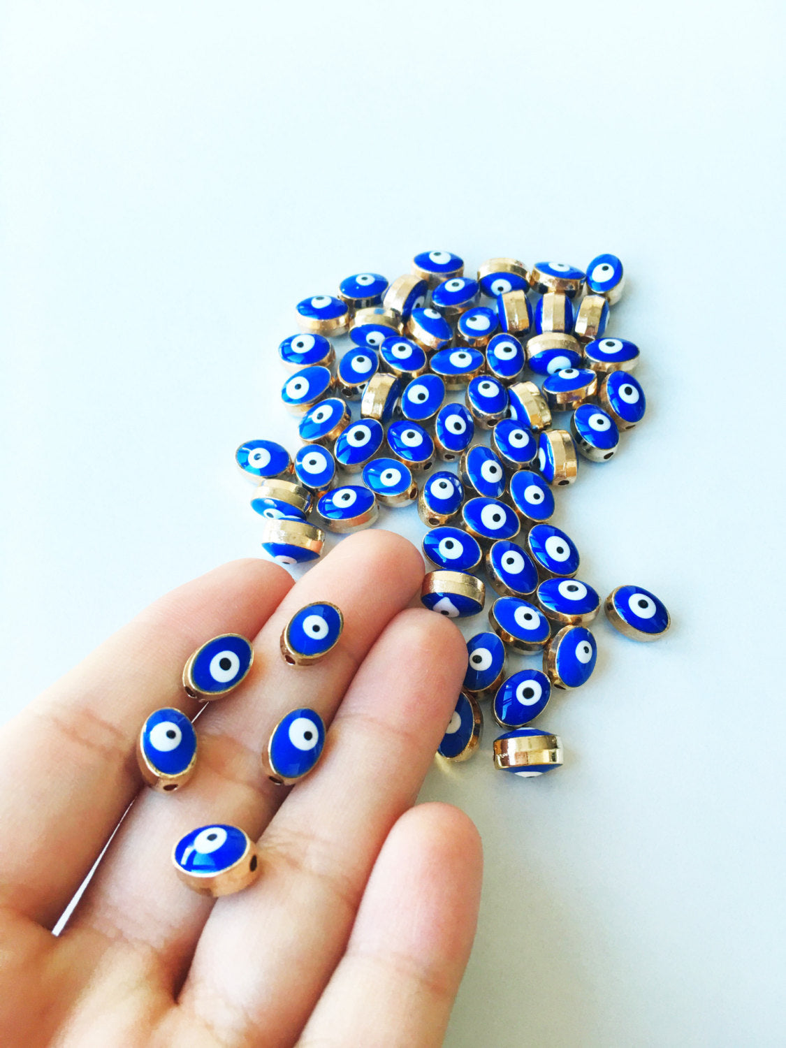 A collection of 5 oval evil eye spacer beads in blue and gold, measuring 10mm x 8mm, perfect for jewelry making.