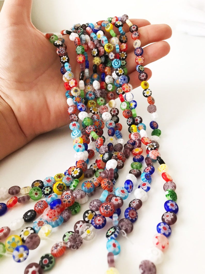 A collection of colorful Millefiori flat coin glass beads in various sizes, showcasing intricate floral designs.