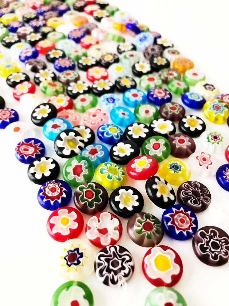 A collection of colorful Millefiori flat coin glass beads in various sizes, showcasing intricate floral designs.