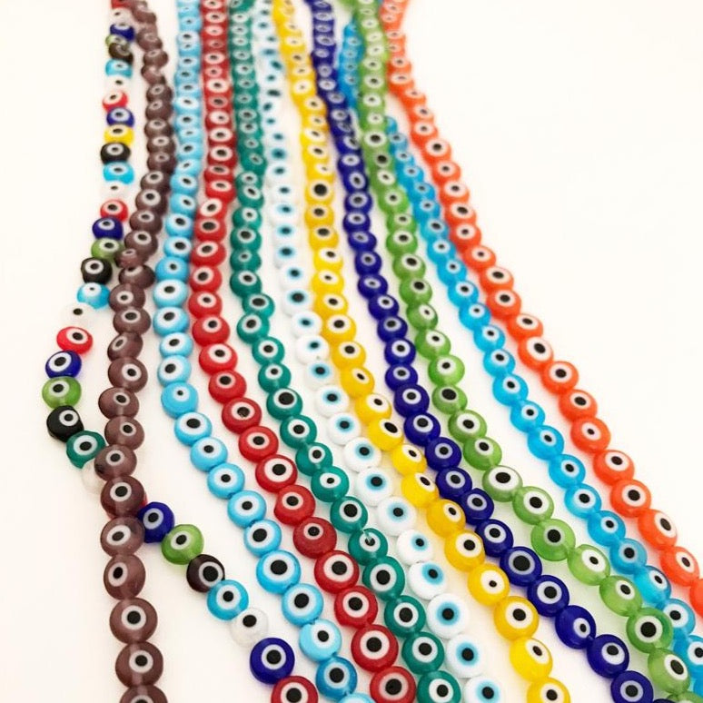 A collection of 6mm to 12mm flat round Evil Eye Glass Beads in various colors, displayed in a hand for size reference.