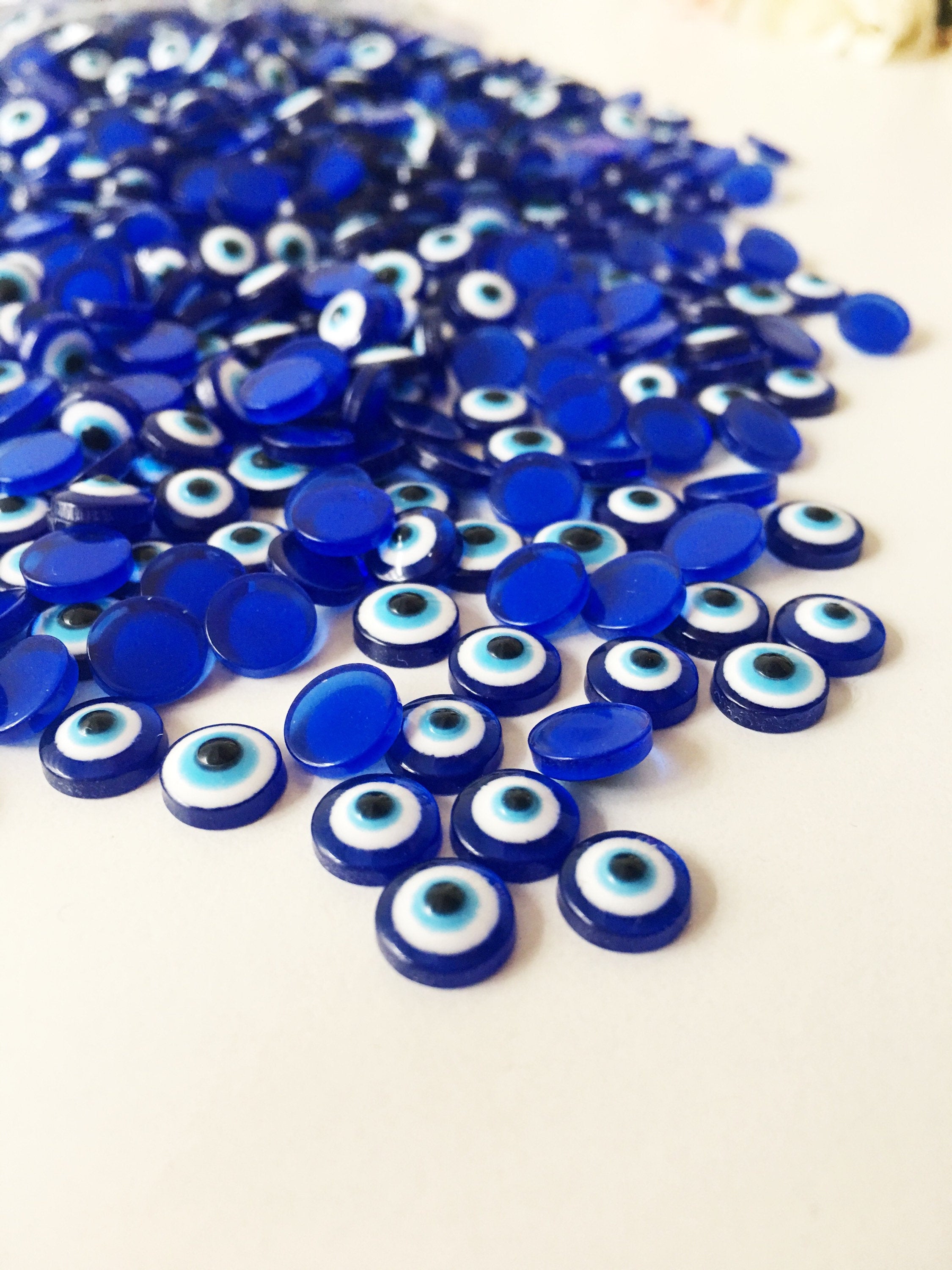 A pack of 20 blue 8mm evil eye cabochons made from resin, showcasing their vibrant color and protective symbol.