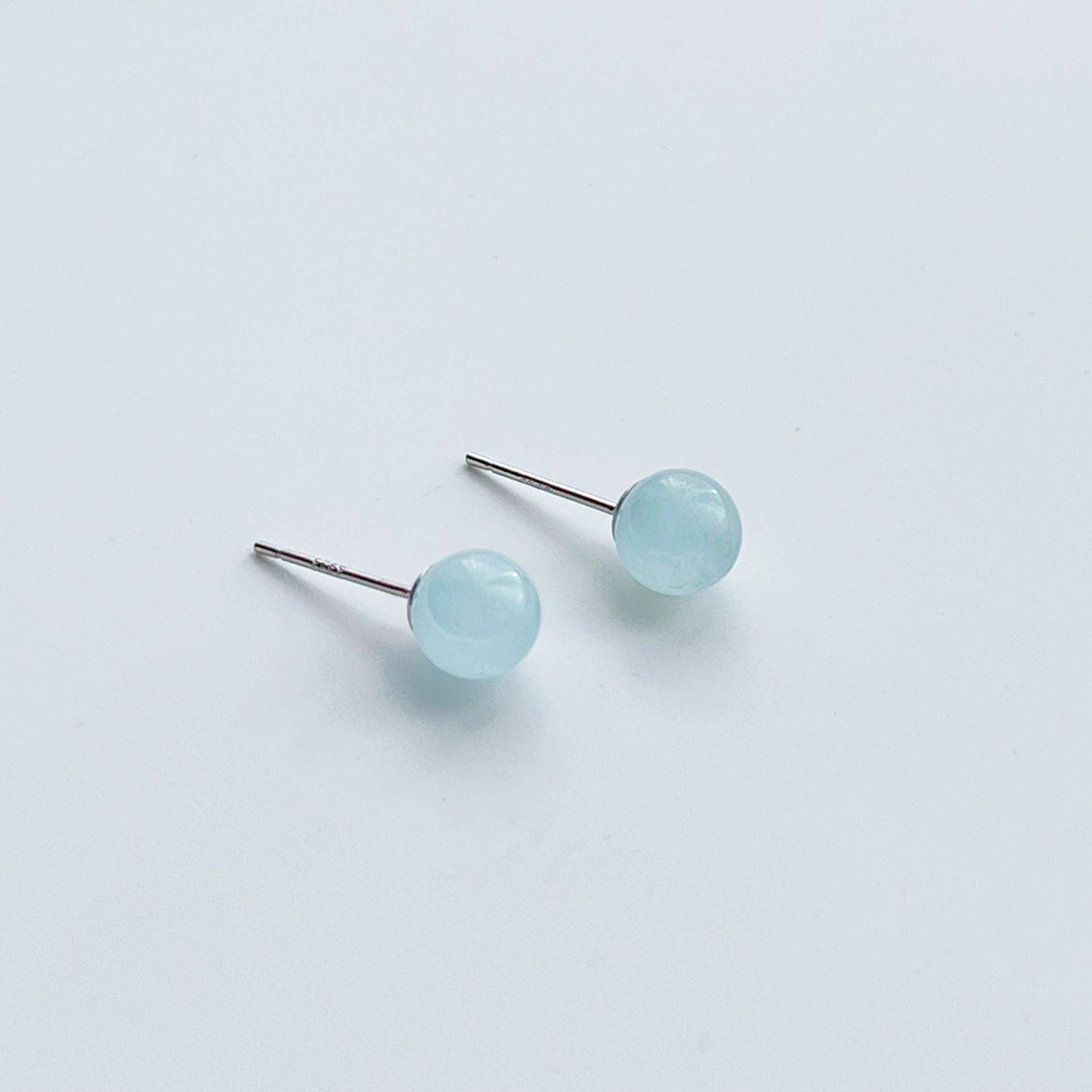 A pair of aquamarine ball shape stud earrings set in sterling silver, showcasing their light blue color and natural beauty.