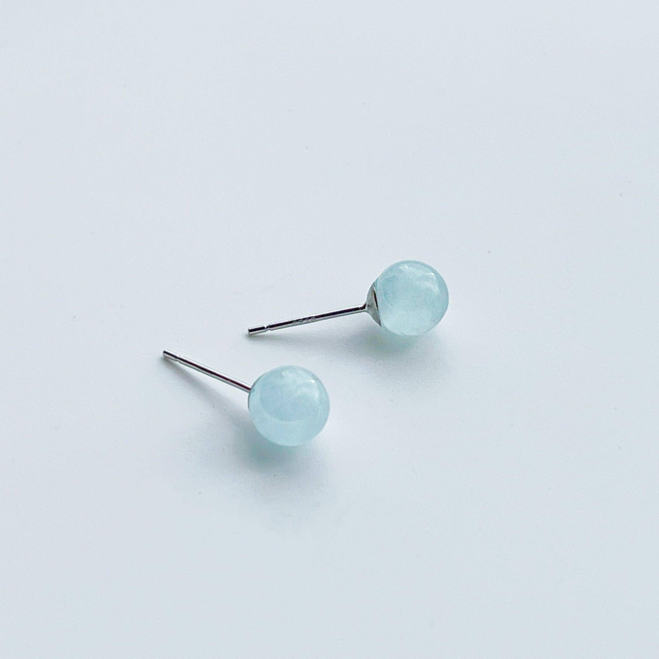 A pair of aquamarine ball shape stud earrings set in sterling silver, showcasing their light blue color and natural beauty.