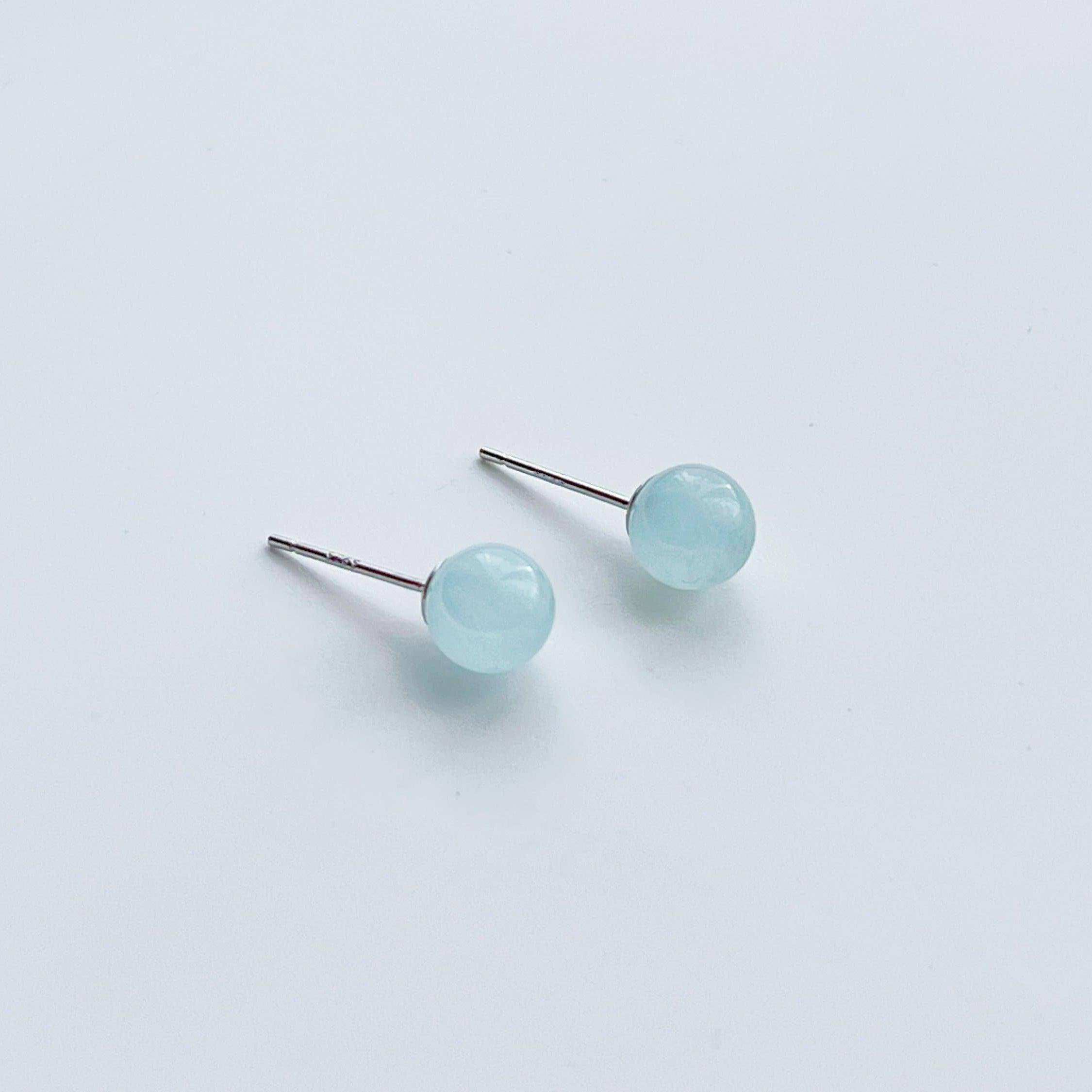 A pair of aquamarine ball shape stud earrings set in sterling silver, showcasing their light blue color and natural beauty.