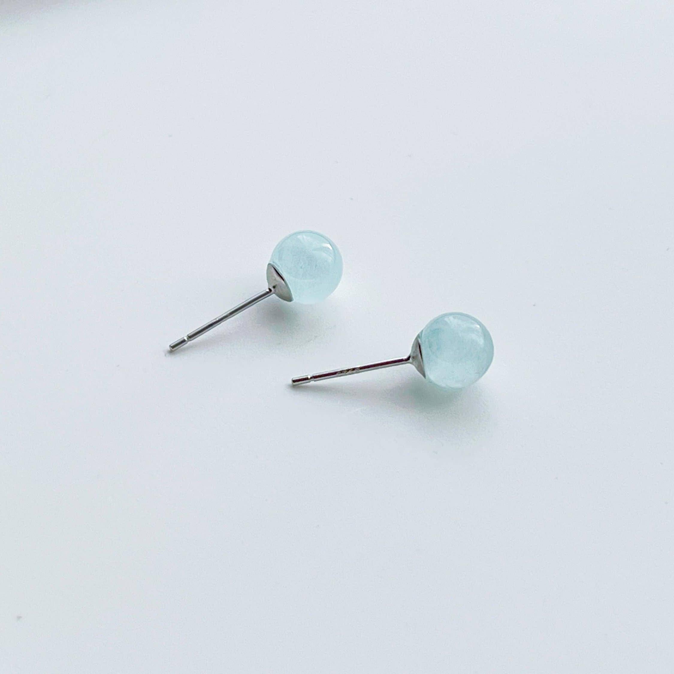 A pair of aquamarine ball shape stud earrings set in sterling silver, showcasing their light blue color and natural beauty.