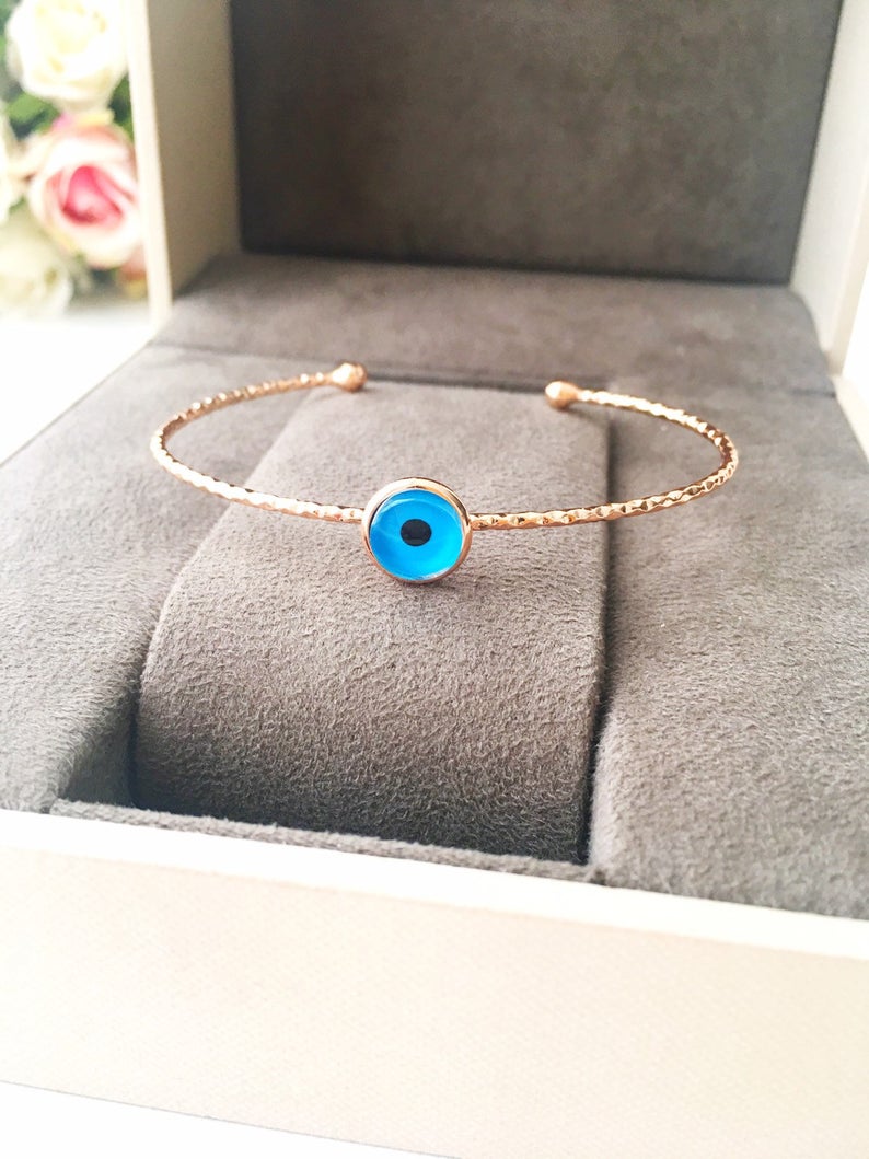 Handmade blue evil eye bangle bracelet with gold accents, featuring an adjustable design and multiple style options.