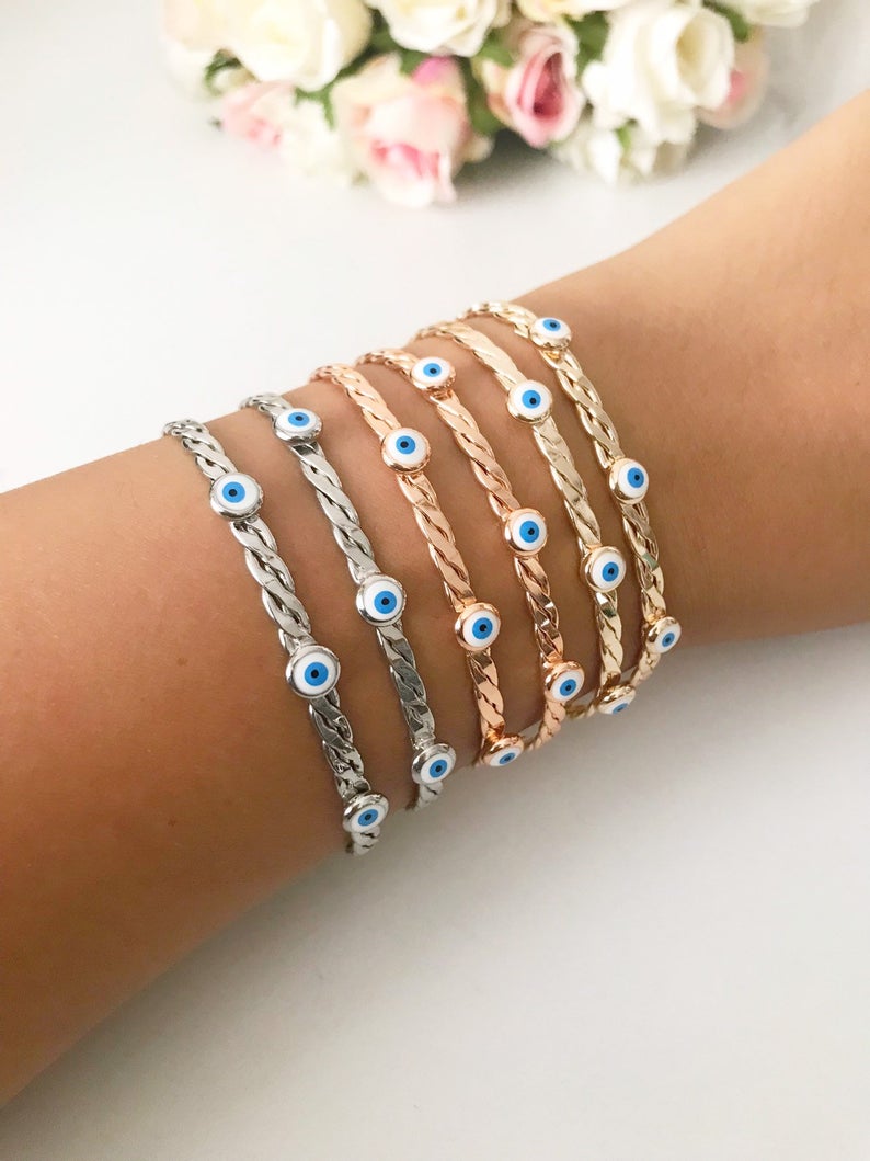 A stylish white evil eye bead bangle bracelet with a movable charm, showcasing its adjustable design and stainless steel material.