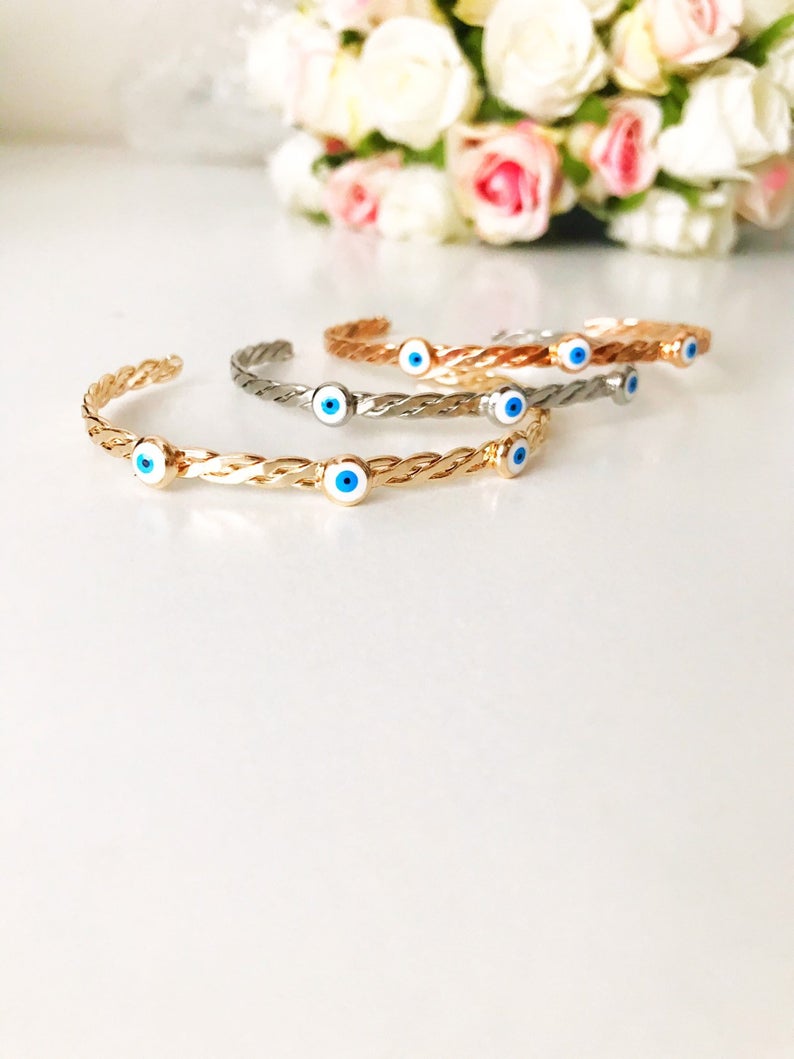 A stylish white evil eye bead bangle bracelet with a movable charm, showcasing its adjustable design and stainless steel material.