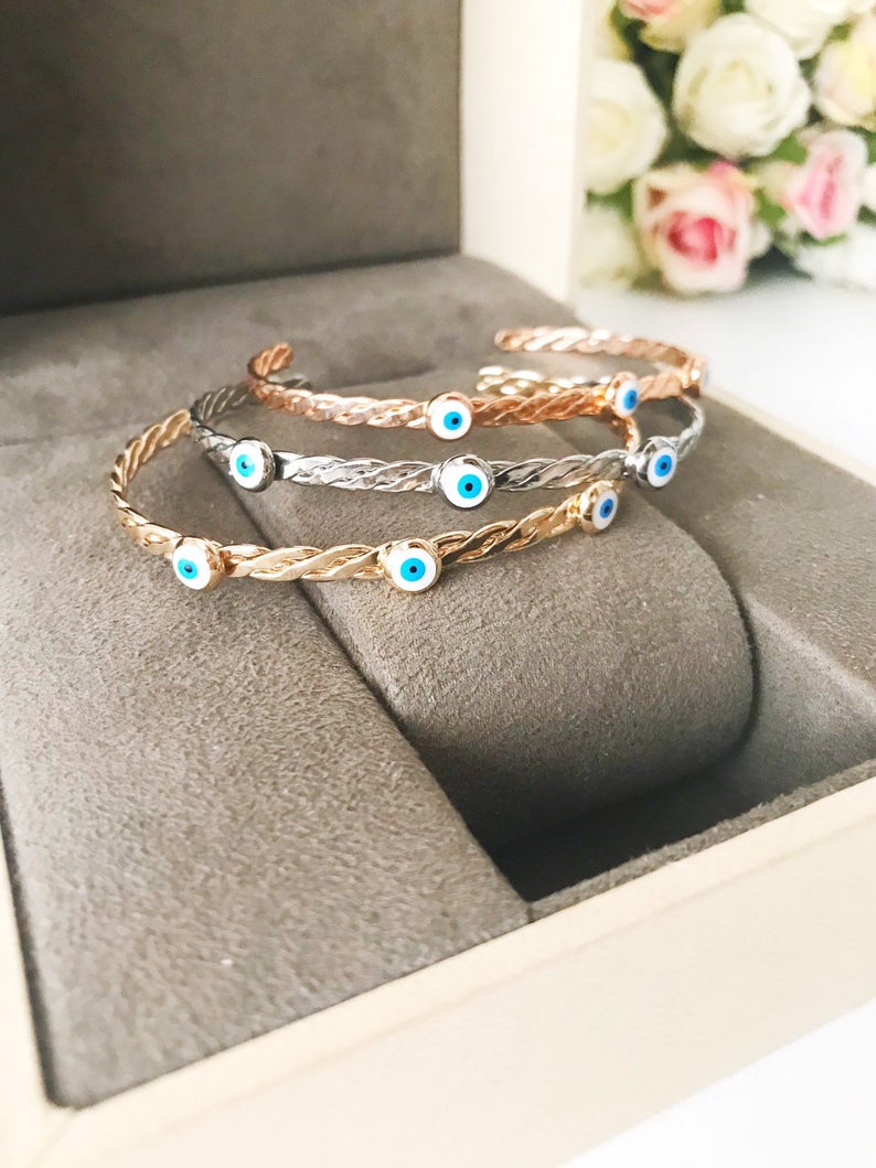 A stylish white evil eye bead bangle bracelet with a movable charm, showcasing its adjustable design and stainless steel material.