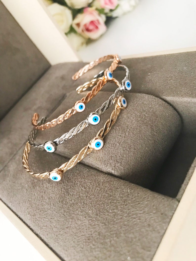 A stylish white evil eye bead bangle bracelet with a movable charm, showcasing its adjustable design and stainless steel material.