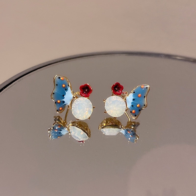 Blue butterfly ear stud featuring a red flower design on a stone background, made from alloy and artificial gemstones.