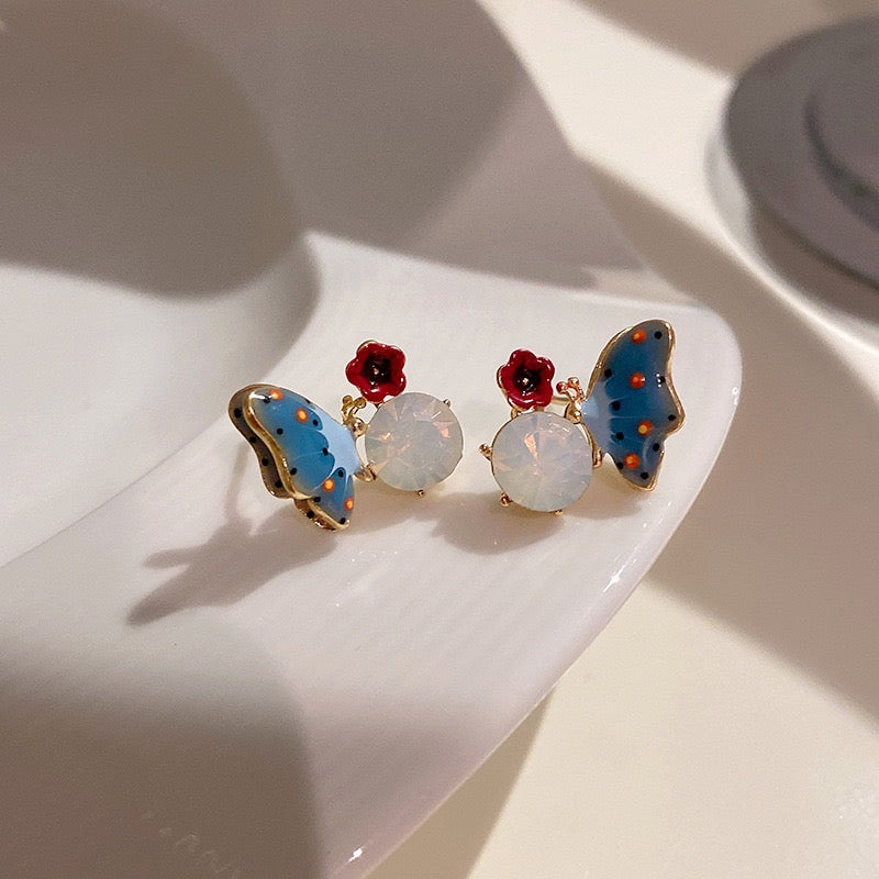 Blue butterfly ear stud featuring a red flower design on a stone background, made from alloy and artificial gemstones.