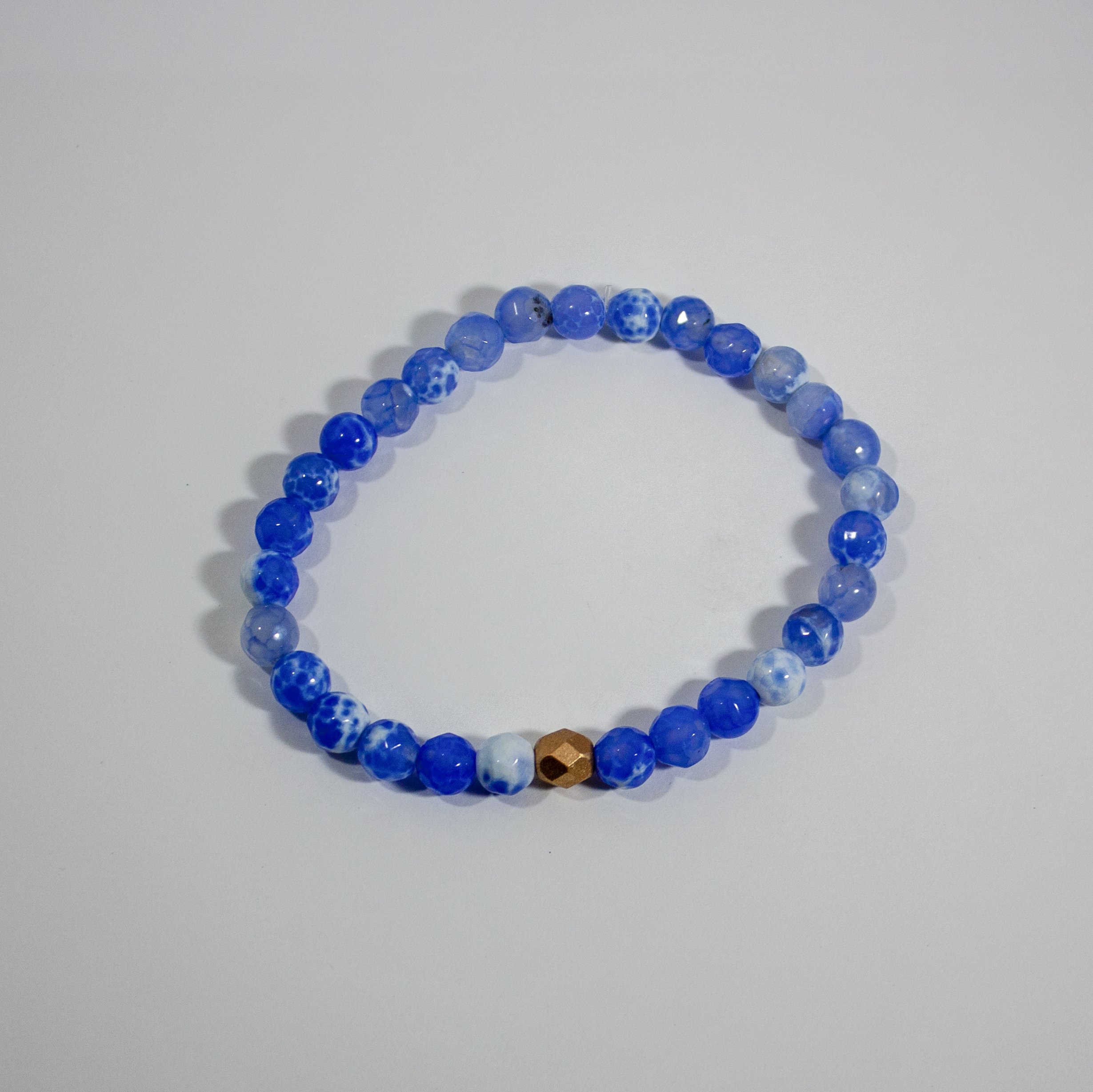 A vibrant blue crackled agate stretch bracelet with gold plated brass accents, showcasing its unique bead patterns.