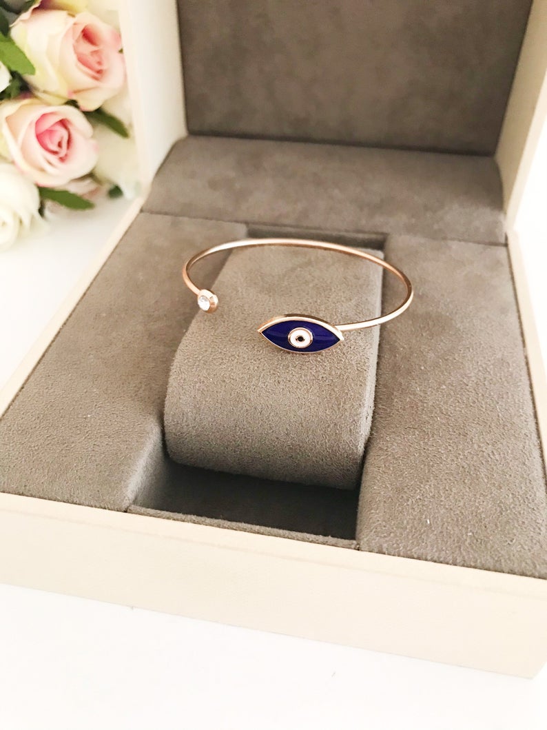 A stylish blue evil eye bracelet featuring a movable charm and rose gold cuff design, made from durable stainless steel.