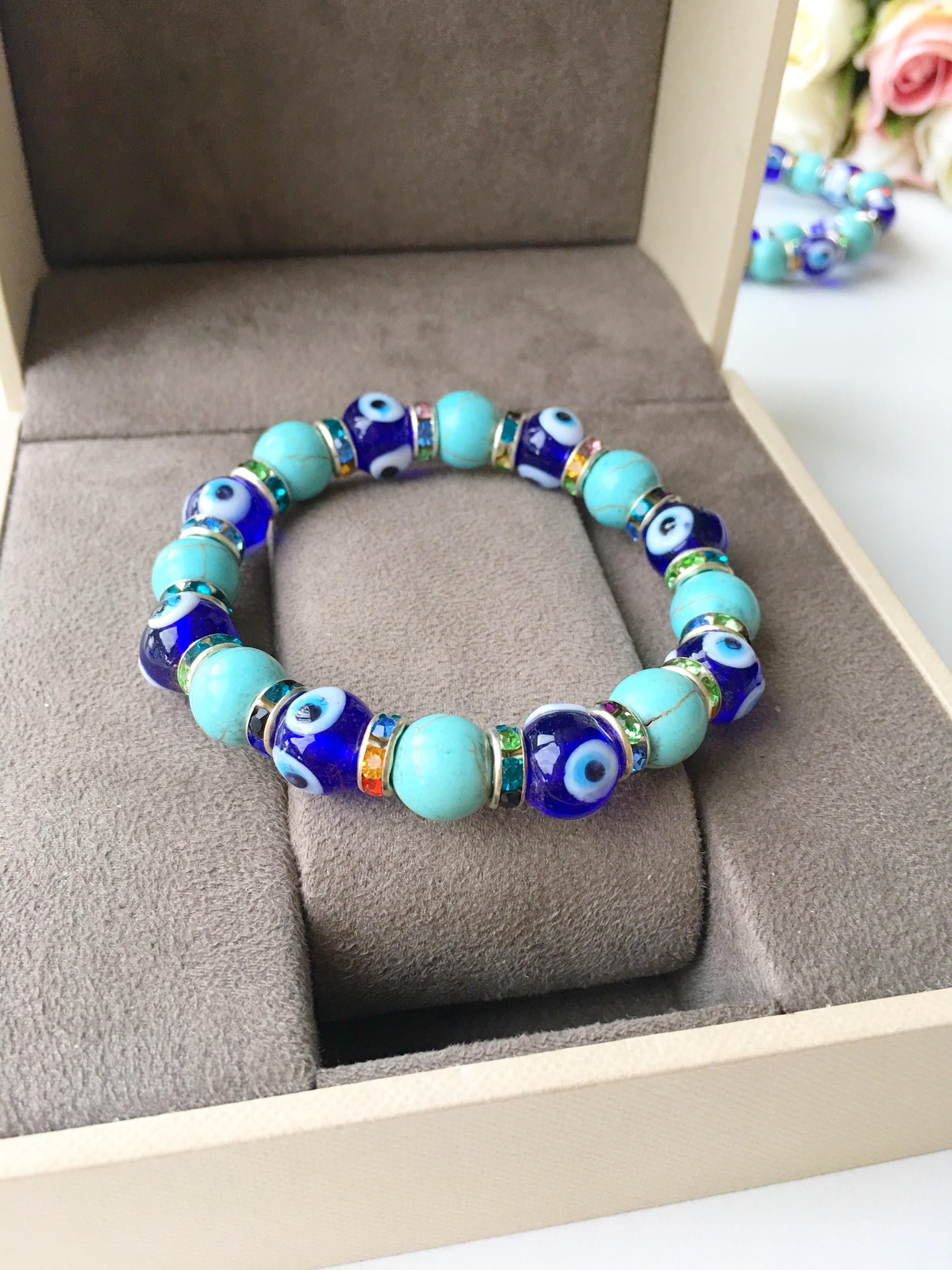 A beautiful blue evil eye bracelet made of glass beads, featuring turquoise accents and a protective charm, elegantly displayed on a soft surface.