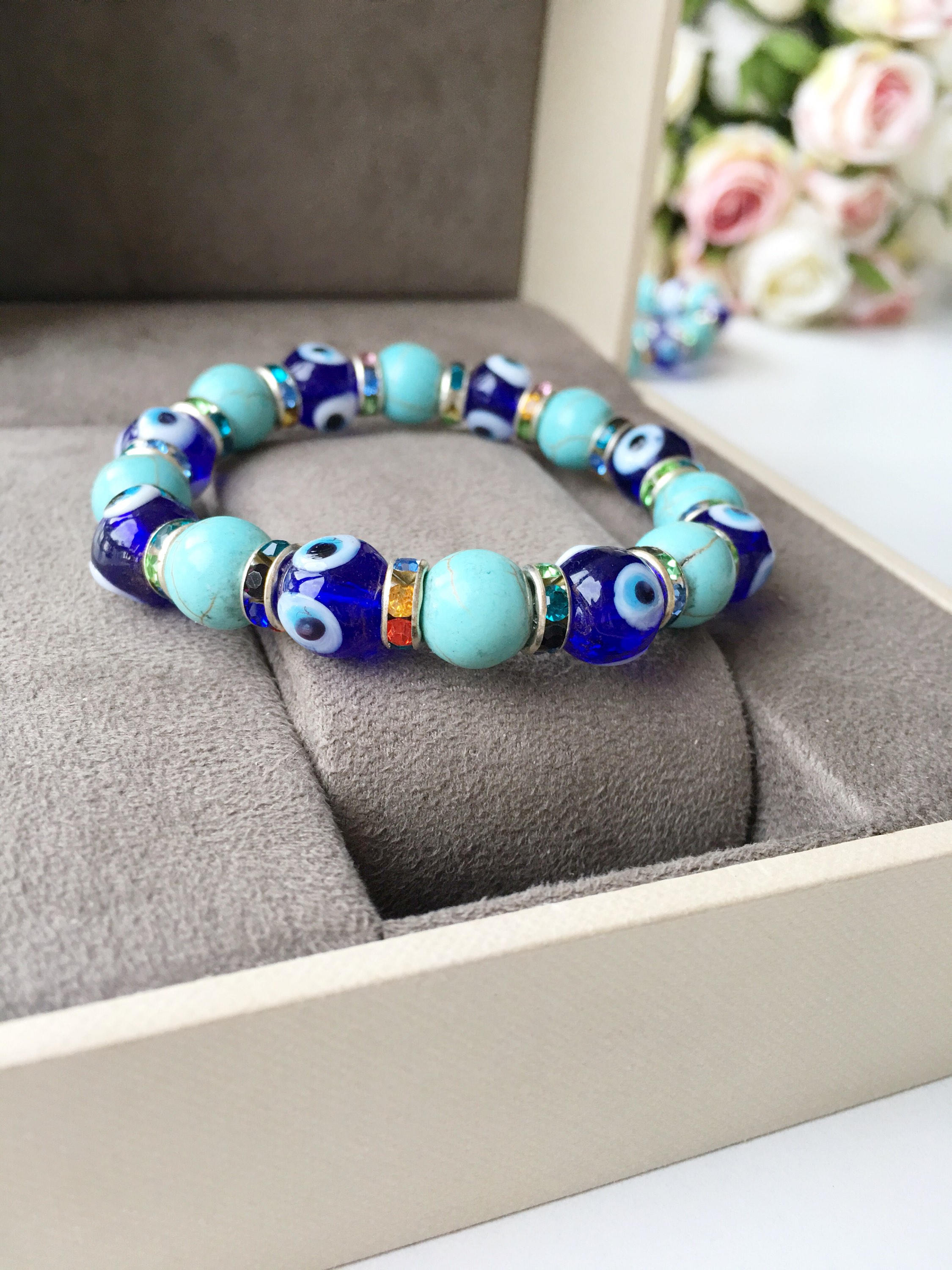 A beautiful blue evil eye bracelet made of glass beads, featuring turquoise accents and a protective charm, elegantly displayed on a soft surface.