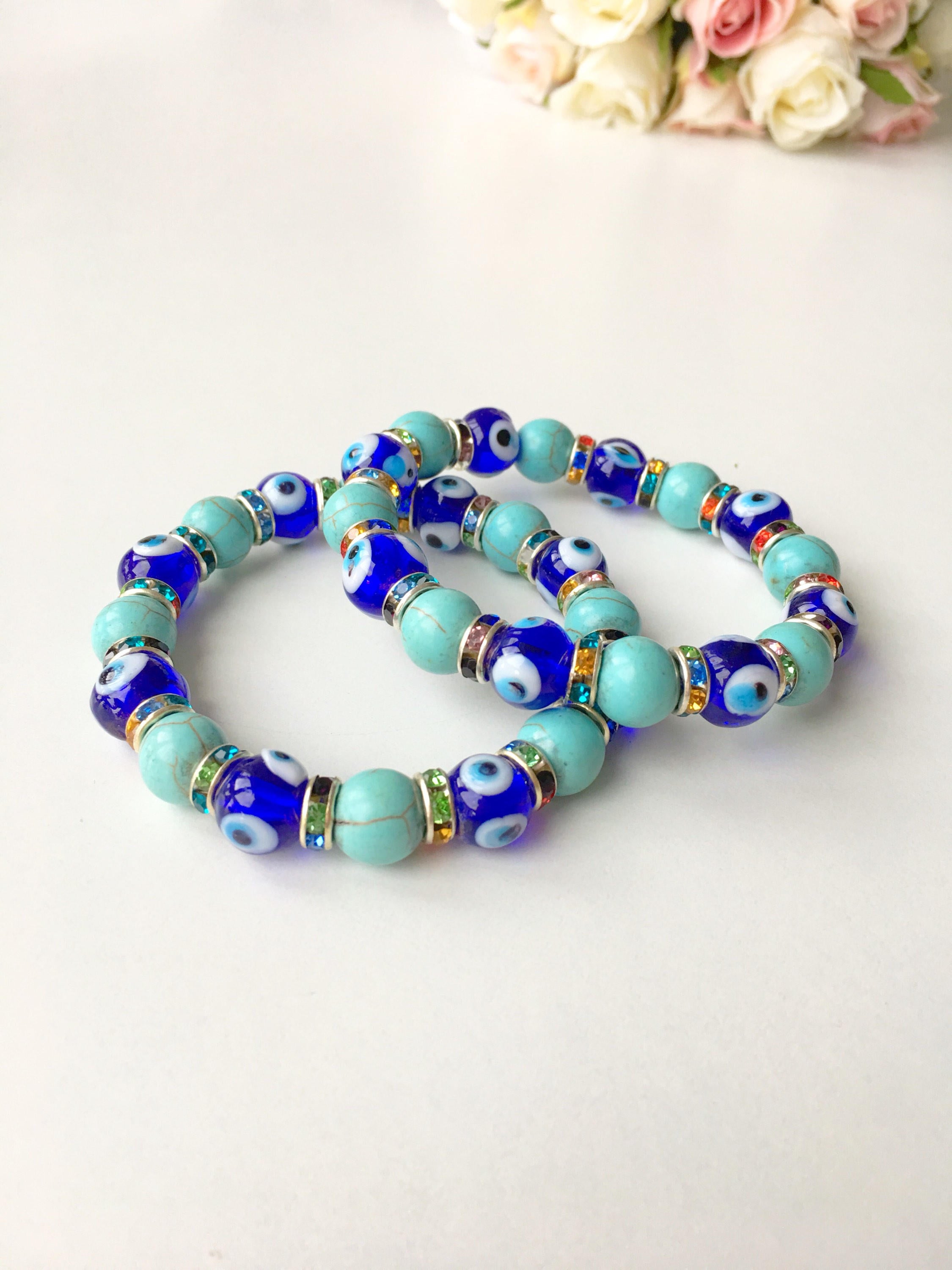 A beautiful blue evil eye bracelet made of glass beads, featuring turquoise accents and a protective charm, elegantly displayed on a soft surface.