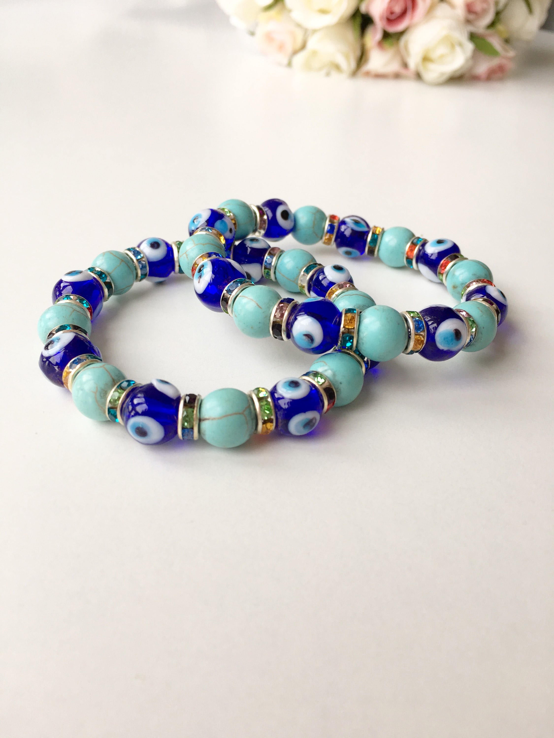 A beautiful blue evil eye bracelet made of glass beads, featuring turquoise accents and a protective charm, elegantly displayed on a soft surface.