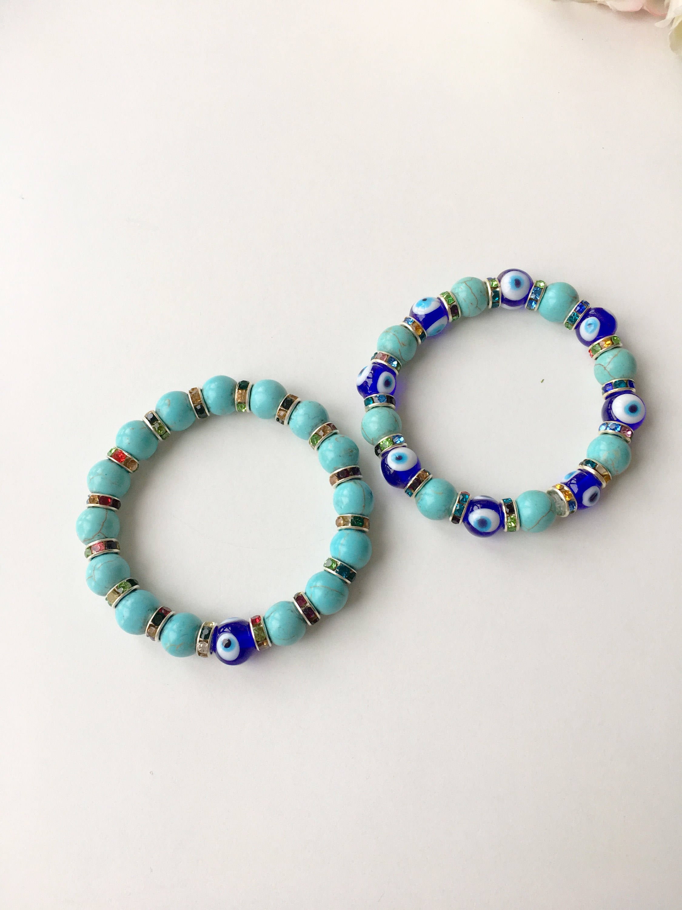 A beautiful blue evil eye bracelet made of glass beads, featuring turquoise accents and a protective charm, elegantly displayed on a soft surface.