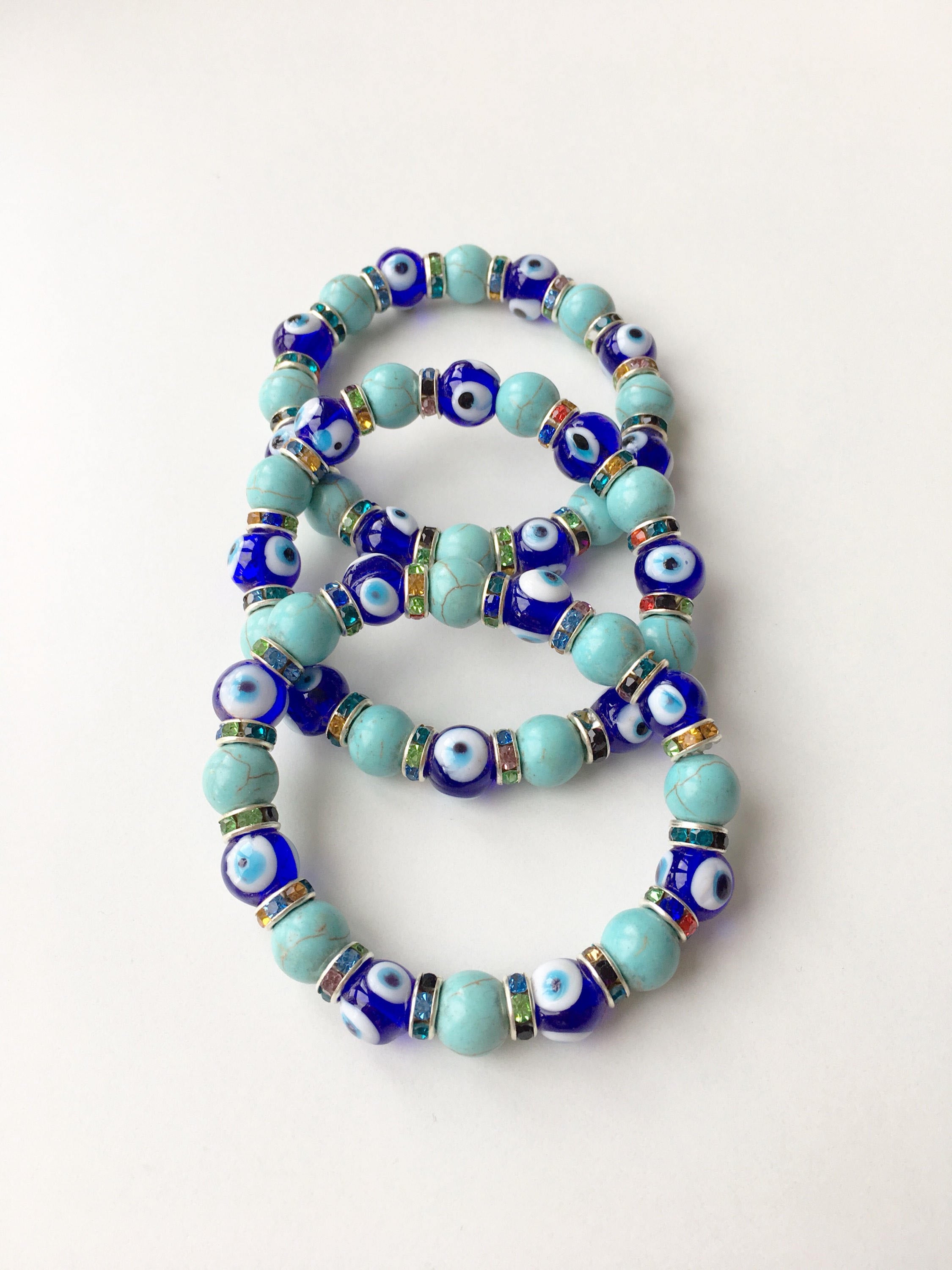 A beautiful blue evil eye bracelet made of glass beads, featuring turquoise accents and a protective charm, elegantly displayed on a soft surface.